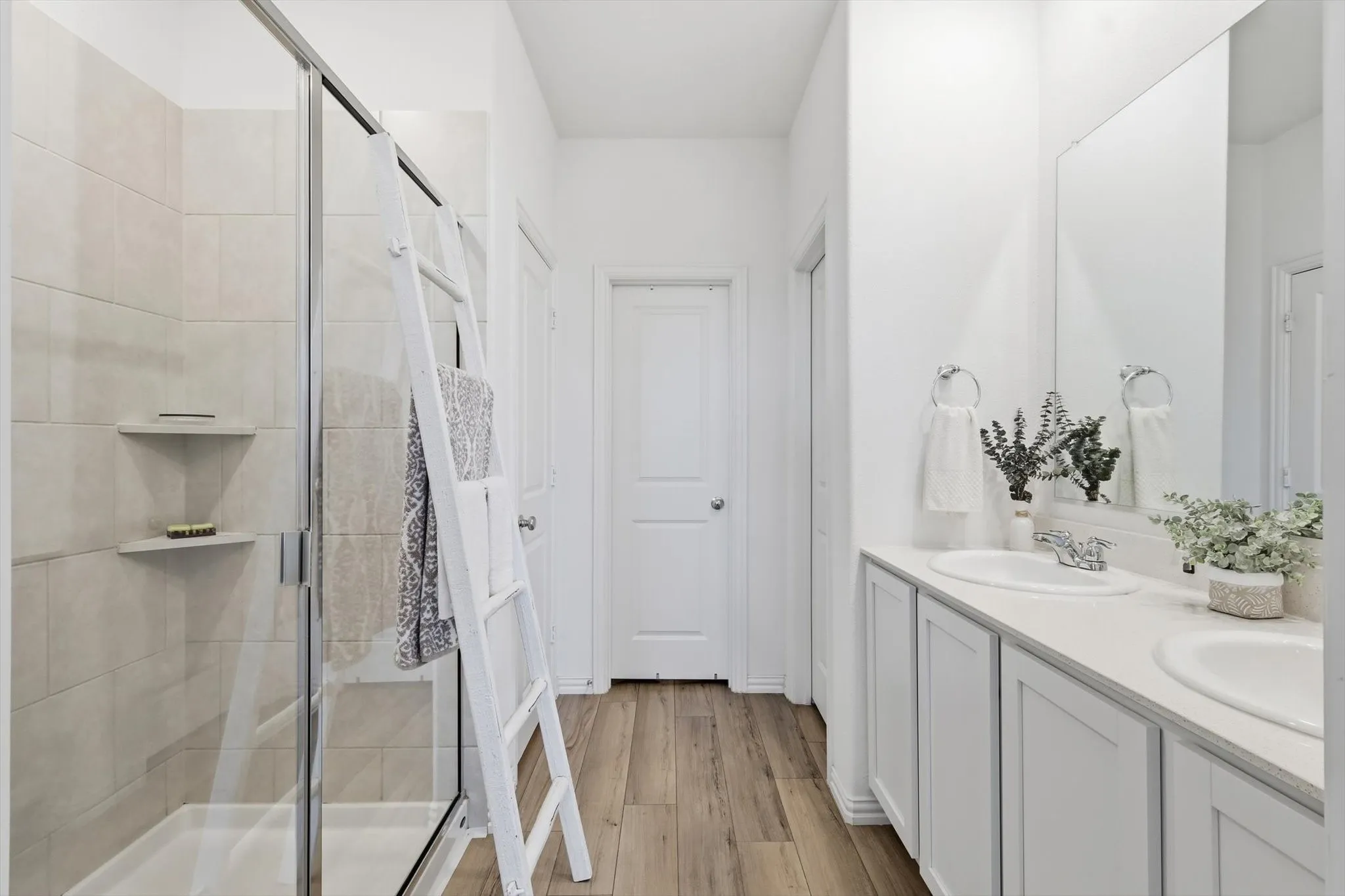 Primary bathroom with light LVP floors, a stall shower, and double vanity