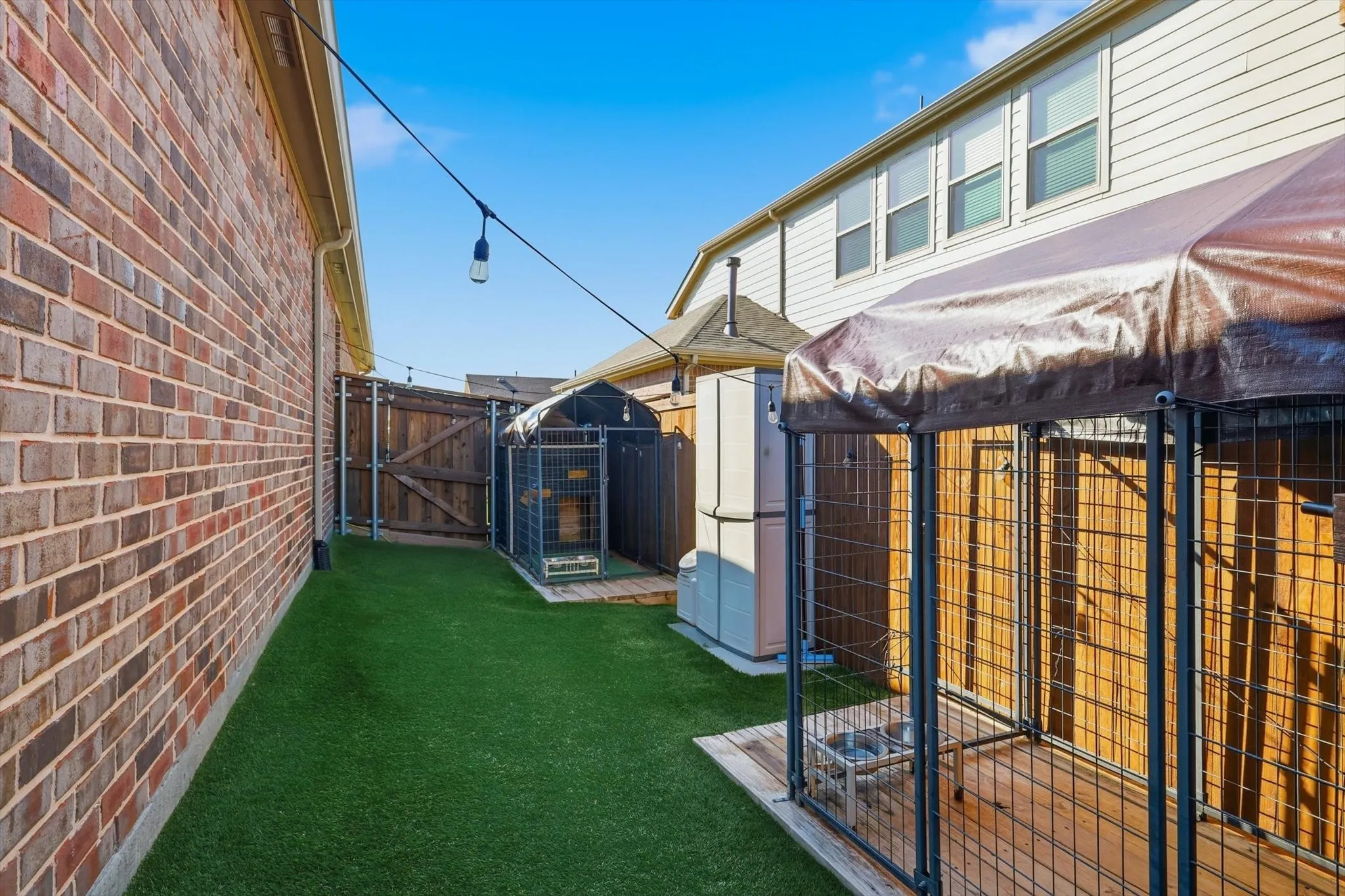 Side yard with lighting, turf and wooden decking, ideal for animals or storage.