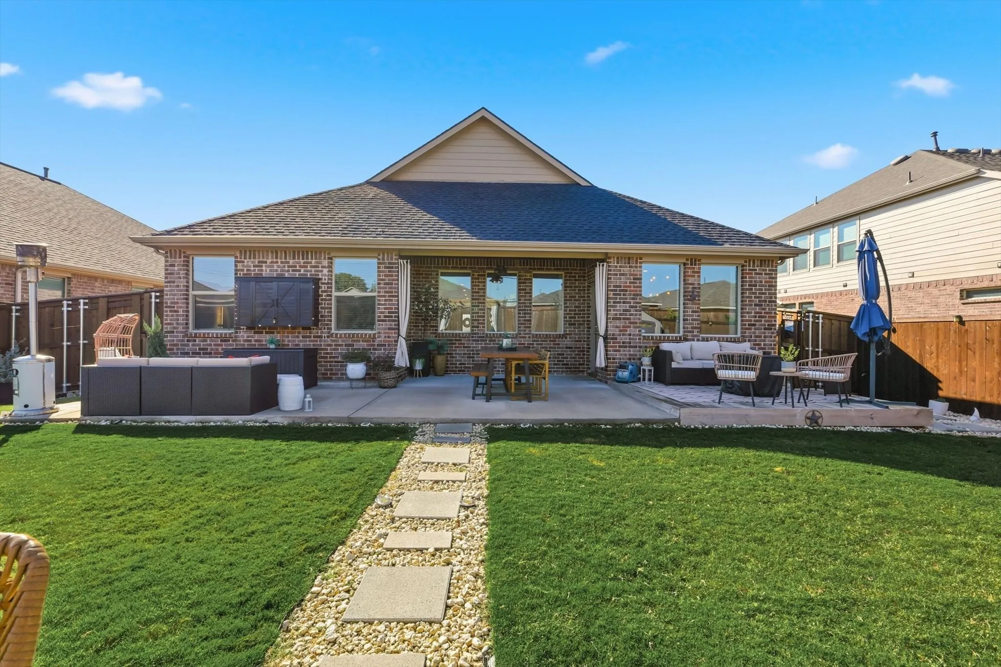 View of fenced backyard, featuring an outdoor kitchen prep area, extended patio and lots of seating options in addition to storage.