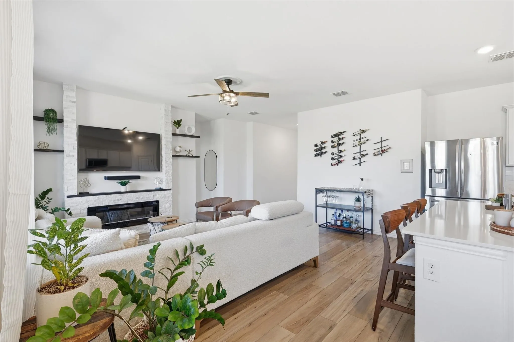 Living room featuring light LVP floors, ceiling fan, and a brand new electric fireplace mounted on a ledger stone accent wall.