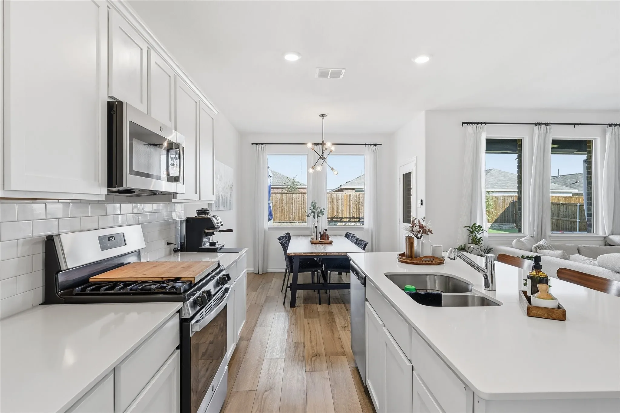 Kitchen with stainless steel appliances, white cabinets, light LVP flooring, a center island with sink, and a chandelier