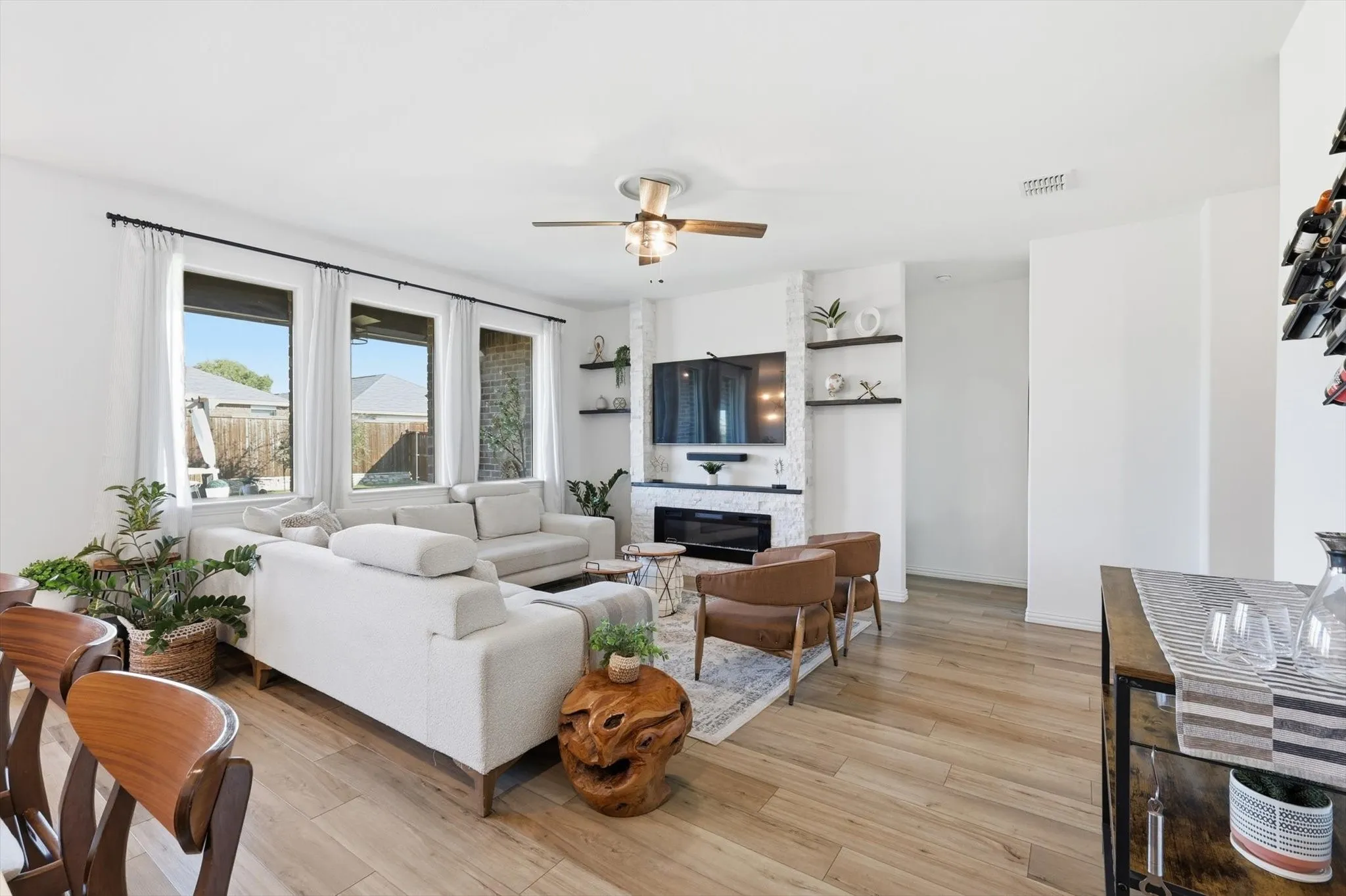 Living room with a ceiling fan, light LVP flooring, and a glass covered fireplace