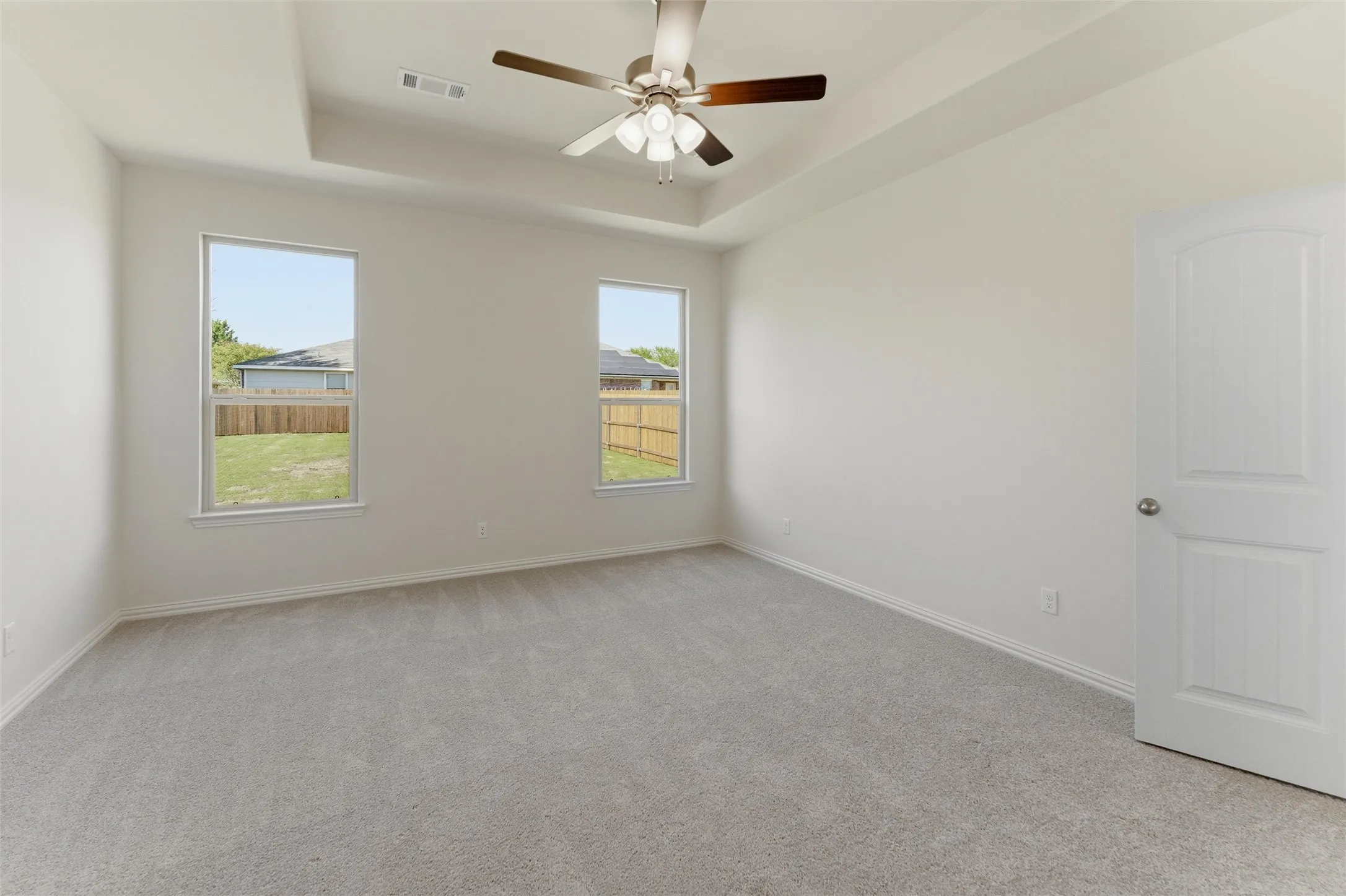 Empty room featuring light carpet, a tray ceiling, and a ceiling fan