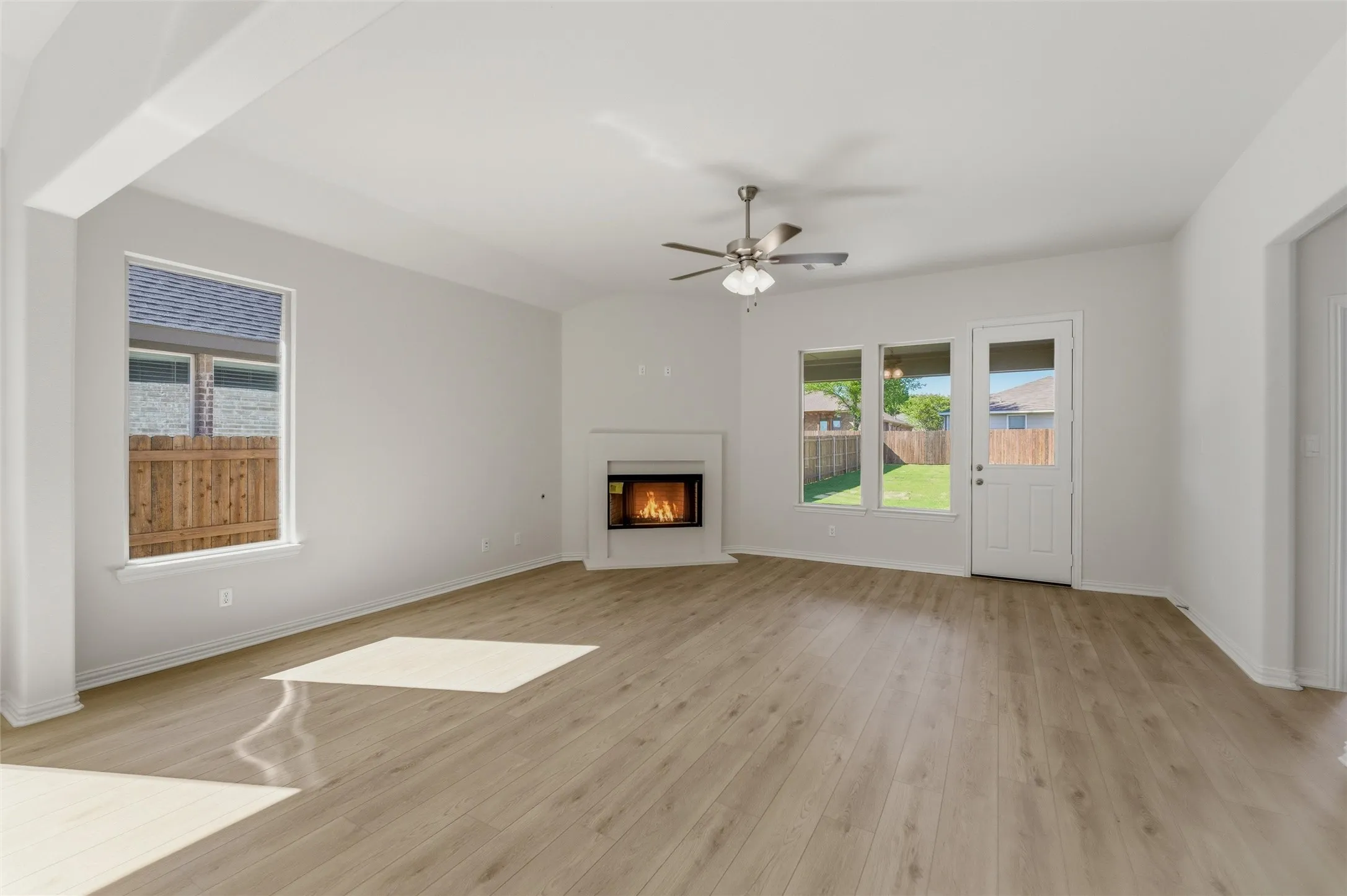 Unfurnished living room with a glass covered fireplace, ceiling fan, light wood-style flooring, and healthy amount of natural light