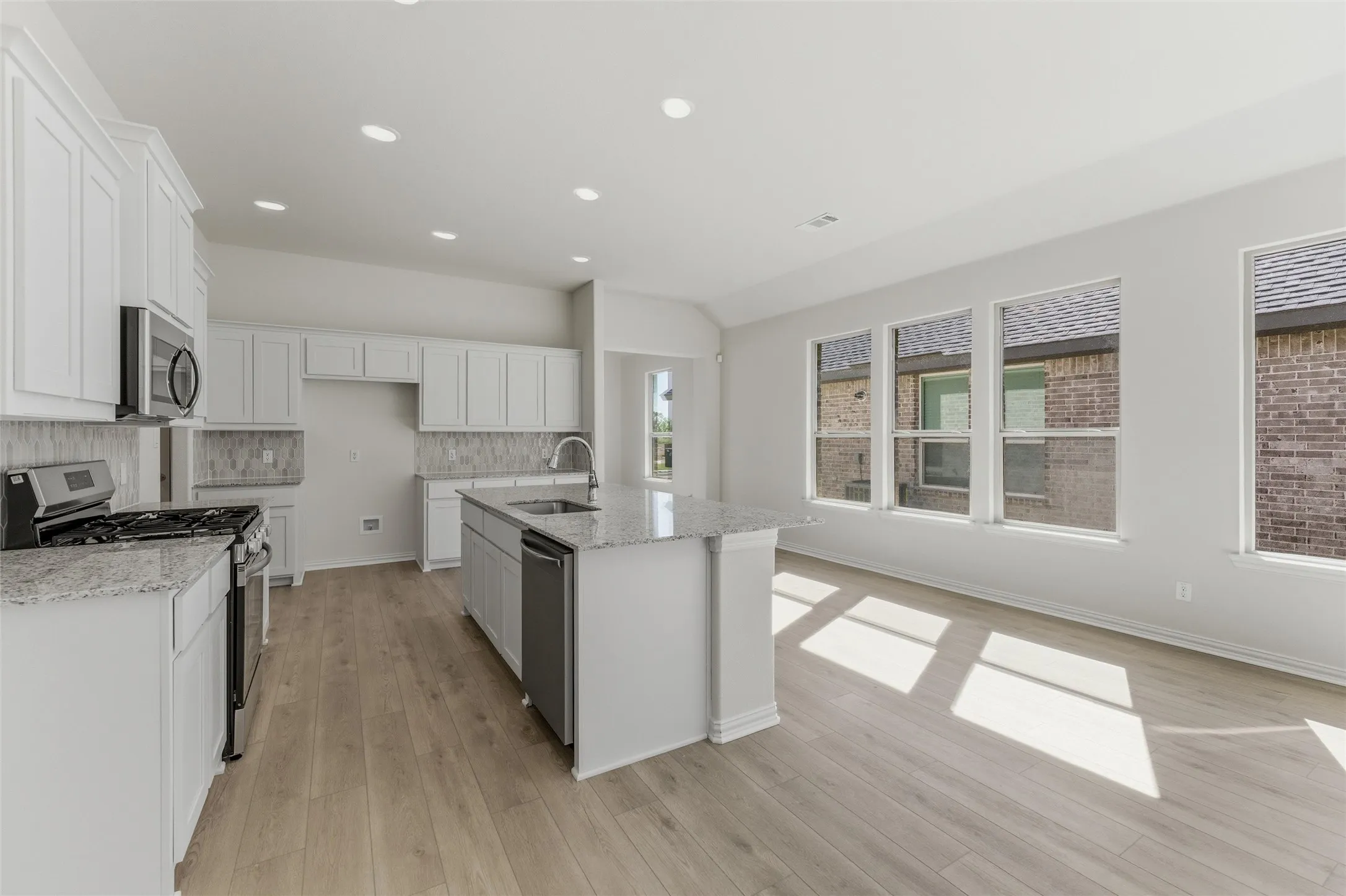 Kitchen featuring stainless steel appliances, white cabinetry, light stone countertops, a center island with sink, and recessed lighting