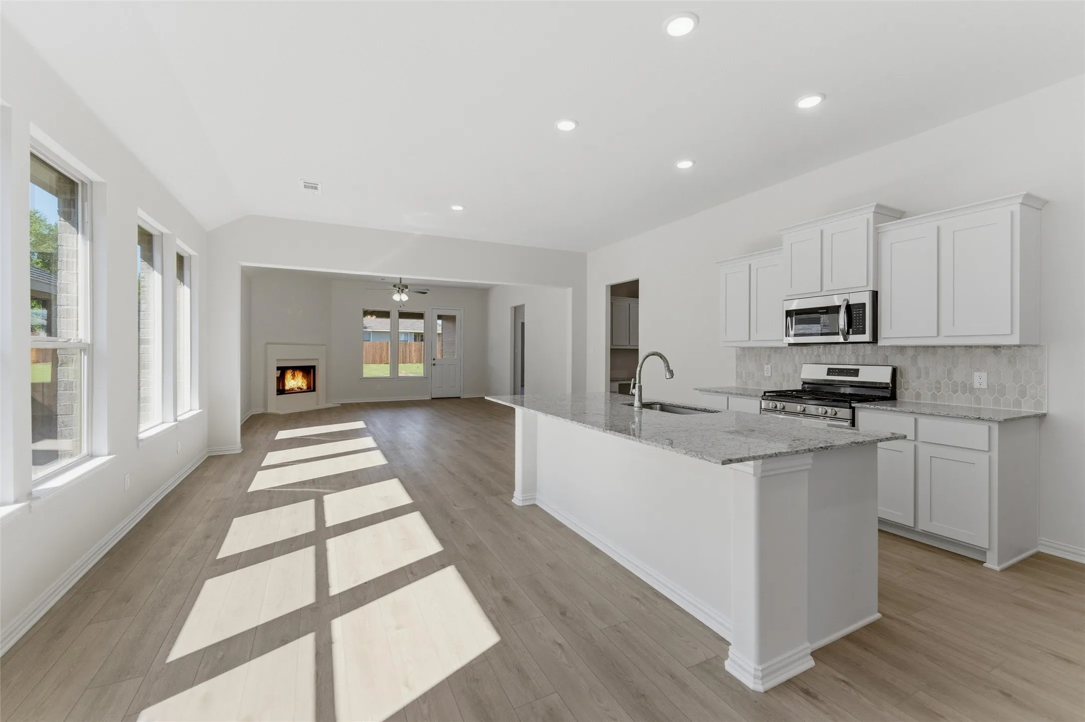 Kitchen with a lit fireplace, white cabinetry, stainless steel appliances, light stone counters, and a center island with sink
