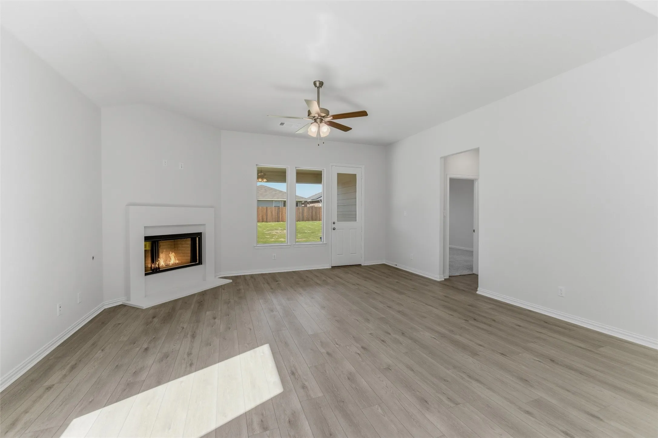Unfurnished living room with a ceiling fan, a glass covered fireplace, and light wood finished floors