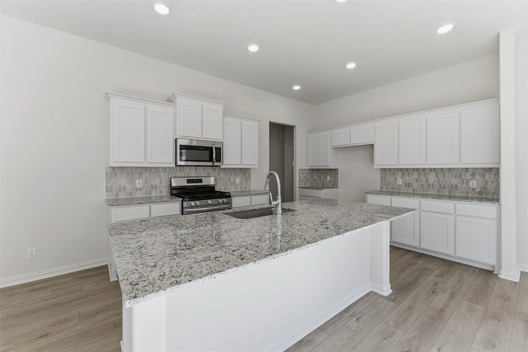Kitchen featuring white cabinets, light stone counters, stainless steel appliances, backsplash, and light wood-style floors