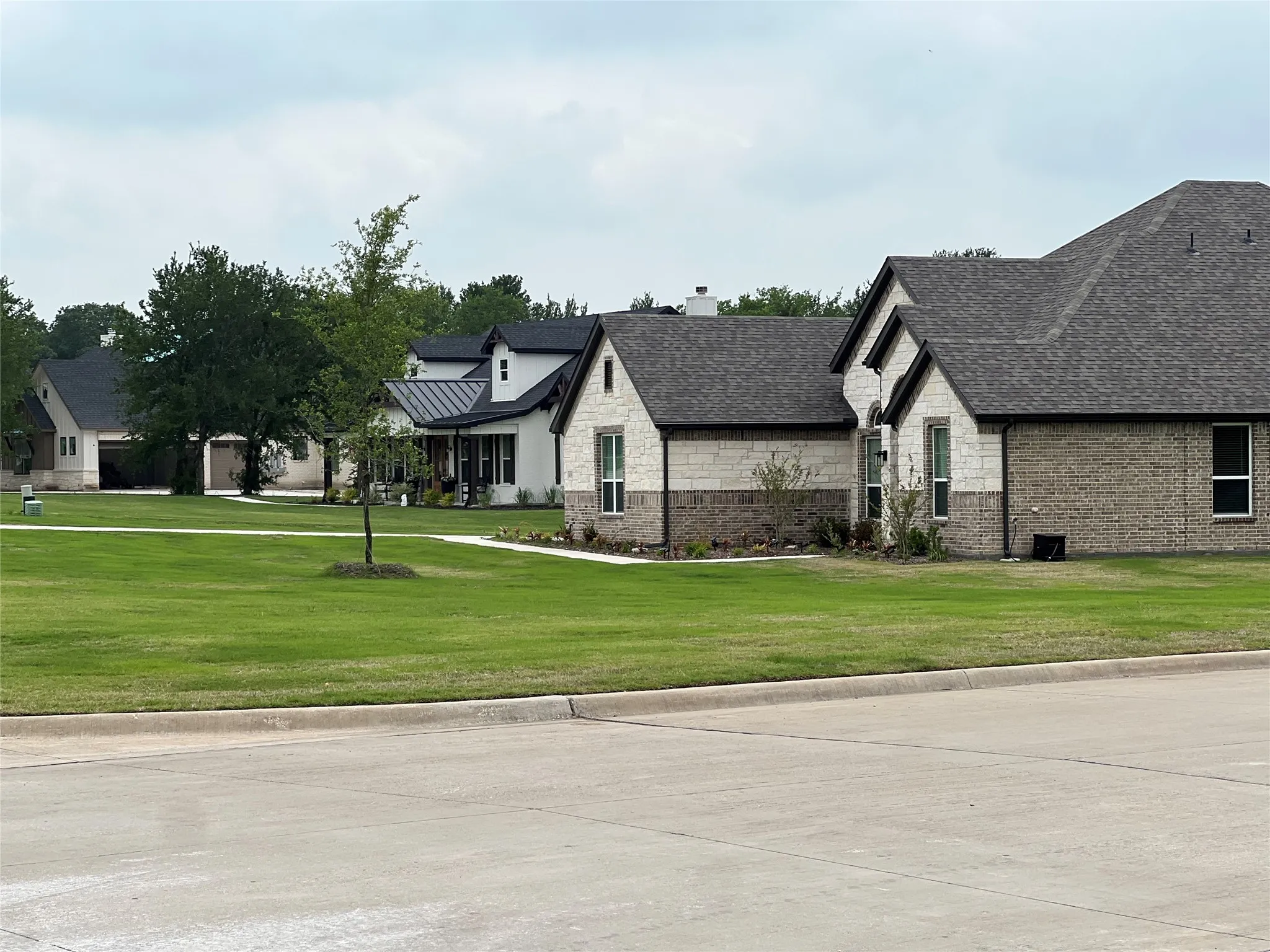 Contemporary architectural style featuring a light stone and brick exterior, dark shingle roofing, and a well-maintained lawn