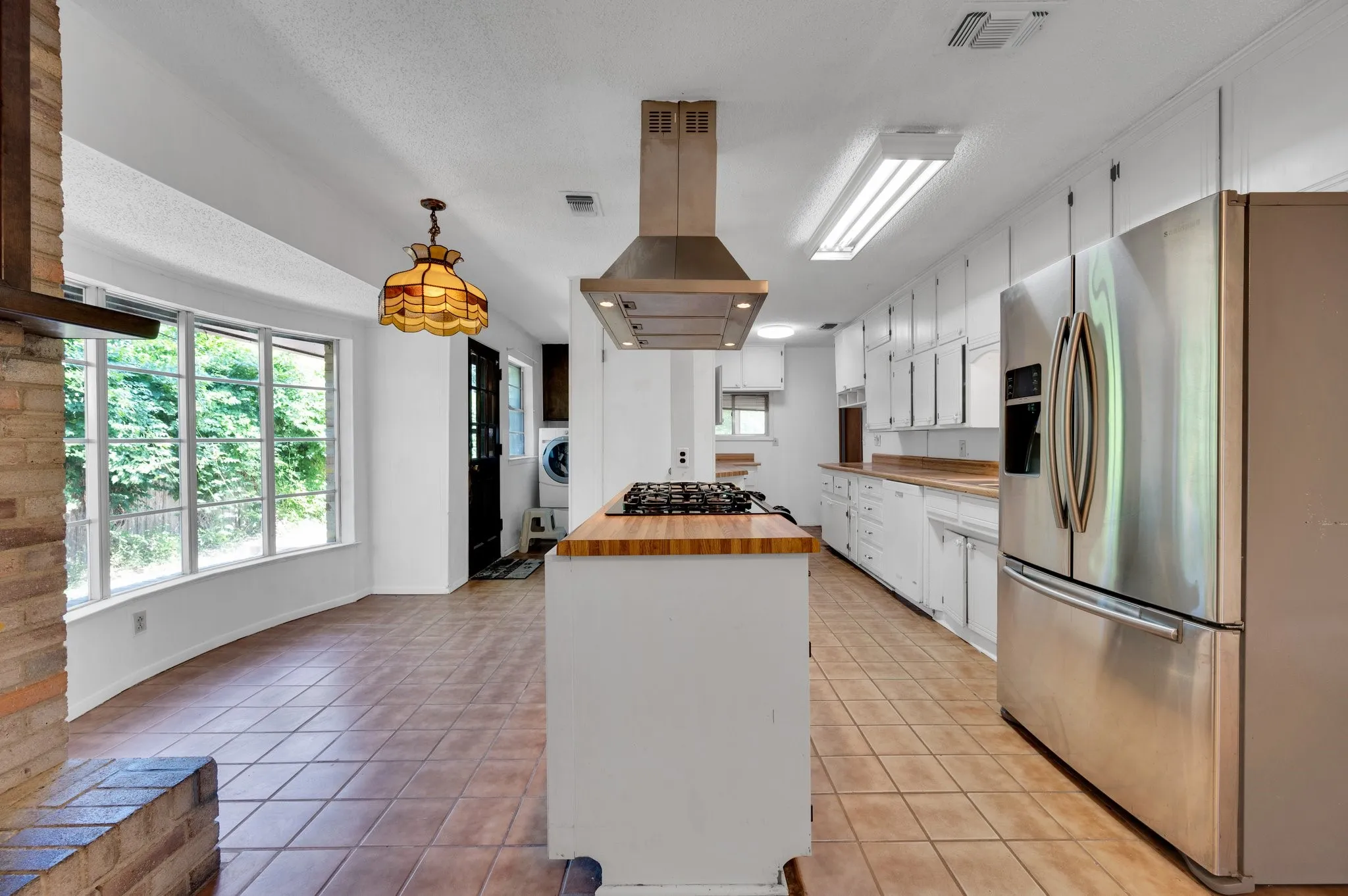 Kitchen featuring butcher block counters, stainless steel fridge, white cabinets, and plenty of natural light