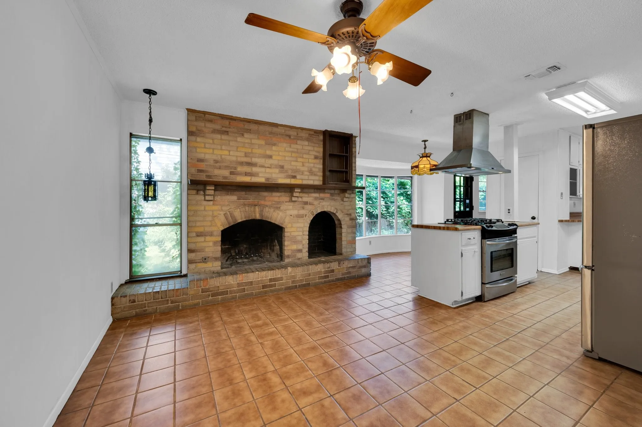 Kitchen with white cabinetry, light tile patterned flooring, island exhaust hood, appliances with stainless steel finishes, and a ceiling fan