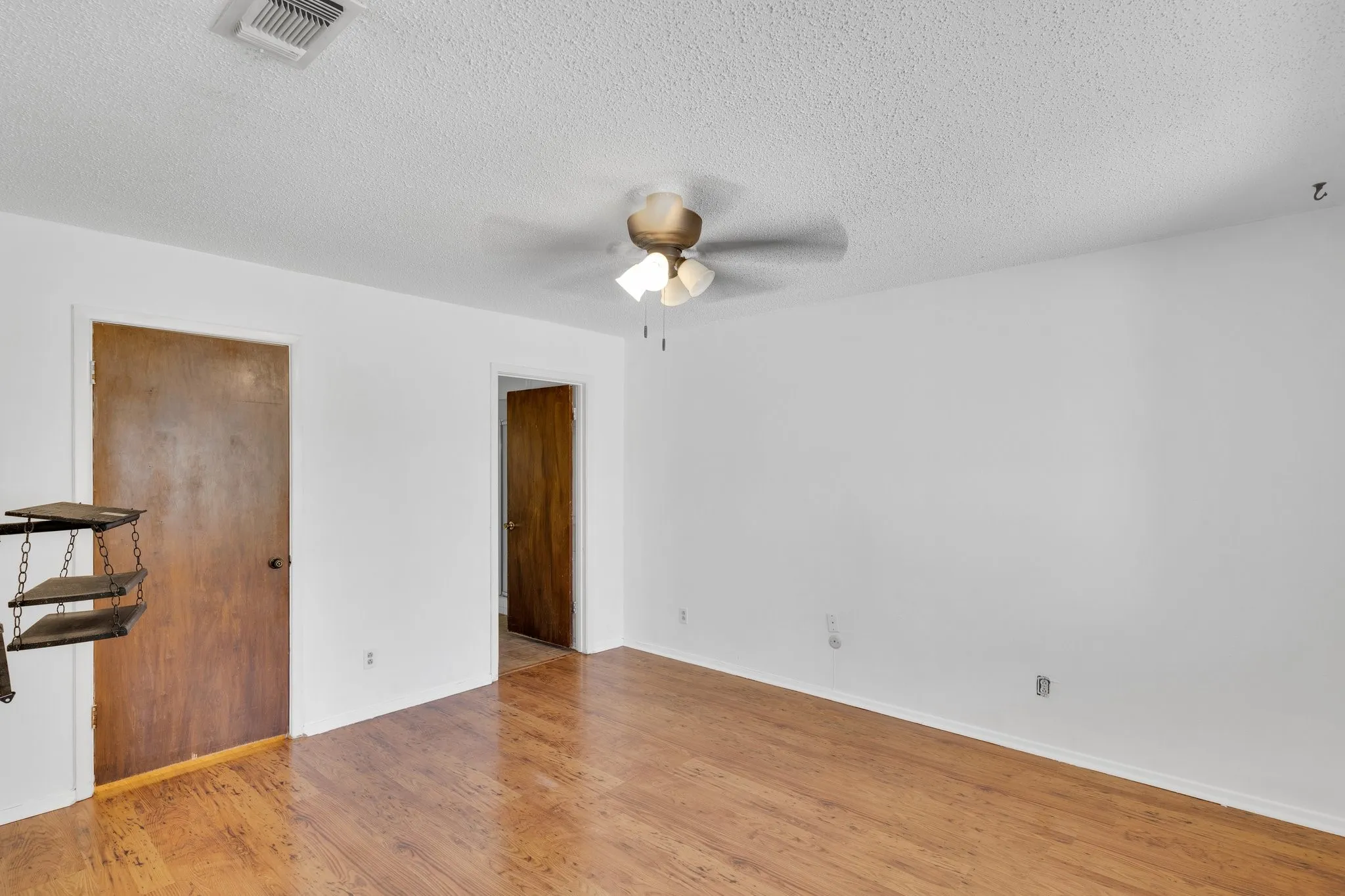 Master bedroom with walk in closet,ceiling fan, light wood-style floors, and a textured ceiling