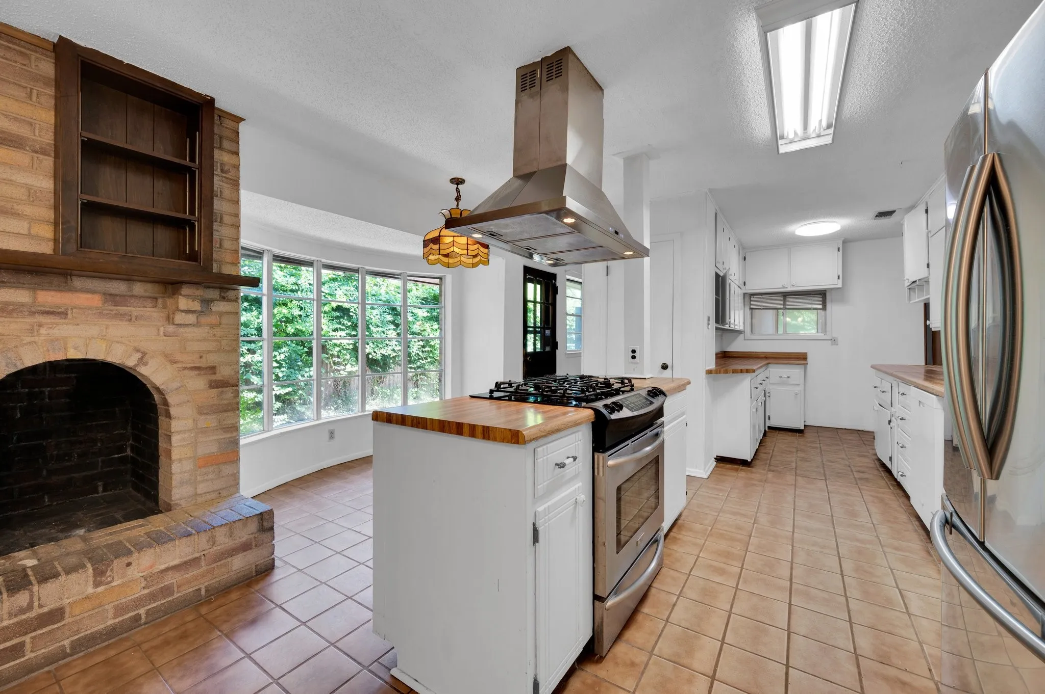 Kitchen with light tile patterned flooring, island range hood, stainless steel appliances, white cabinetry, and a textured ceiling