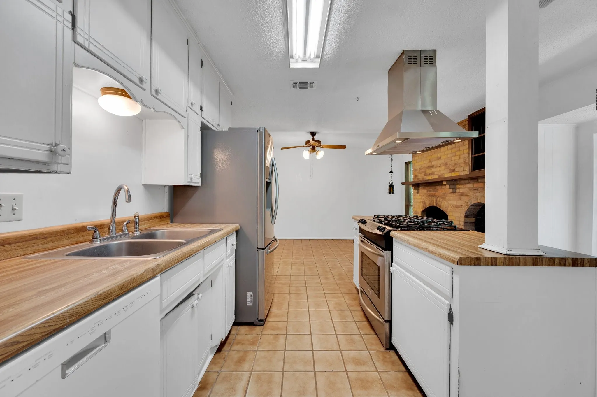 Kitchen with appliances with stainless steel finishes, island exhaust hood, light tile patterned floors, white cabinets, and ceiling fan