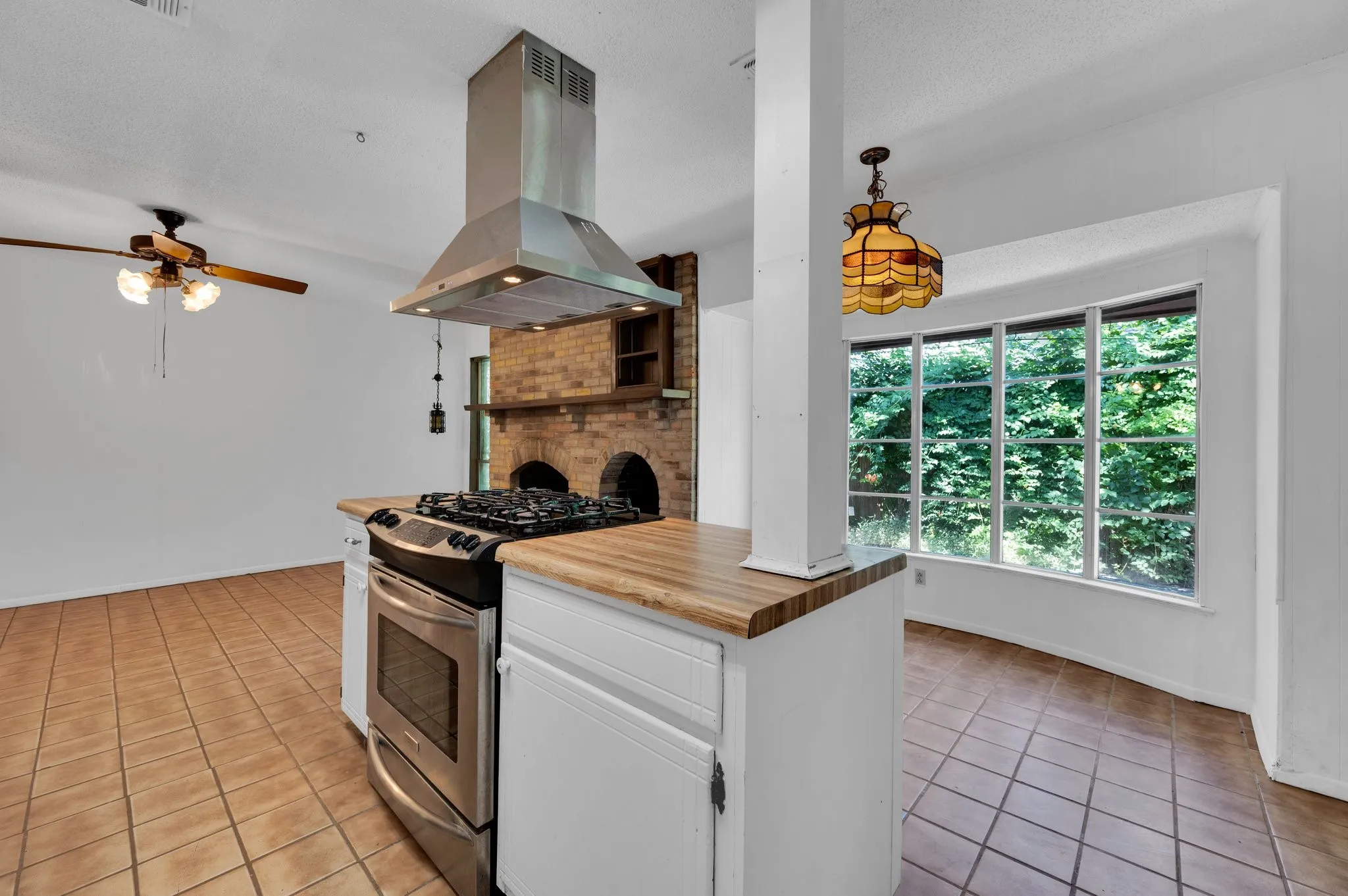 Kitchen featuring light tile patterned floors, island exhaust hood, stainless steel range with gas cooktop, ceiling fan, and white cabinets