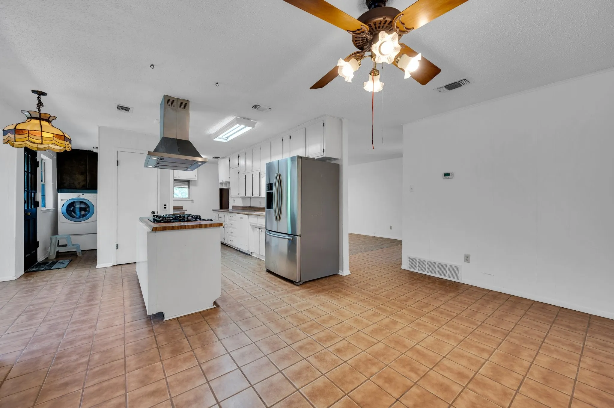 Kitchen with stainless steel fridge, ceiling fan, white cabinets, and island exhaust hood