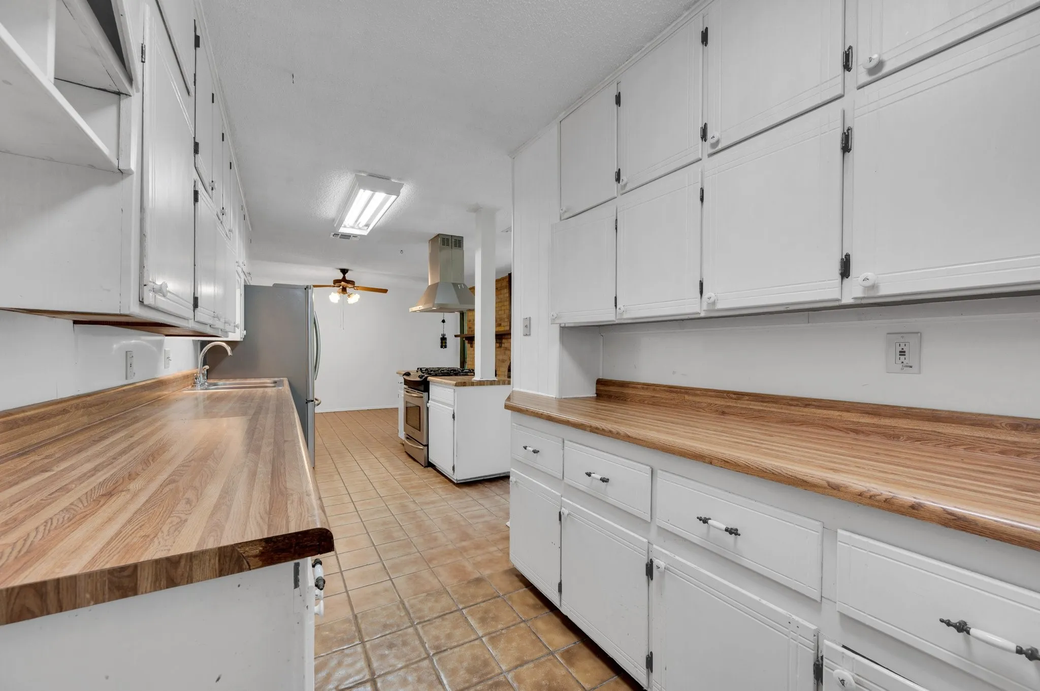 Kitchen featuring white cabinets, island exhaust hood, light tile patterned flooring, ceiling fan, and appliances with stainless steel finishes