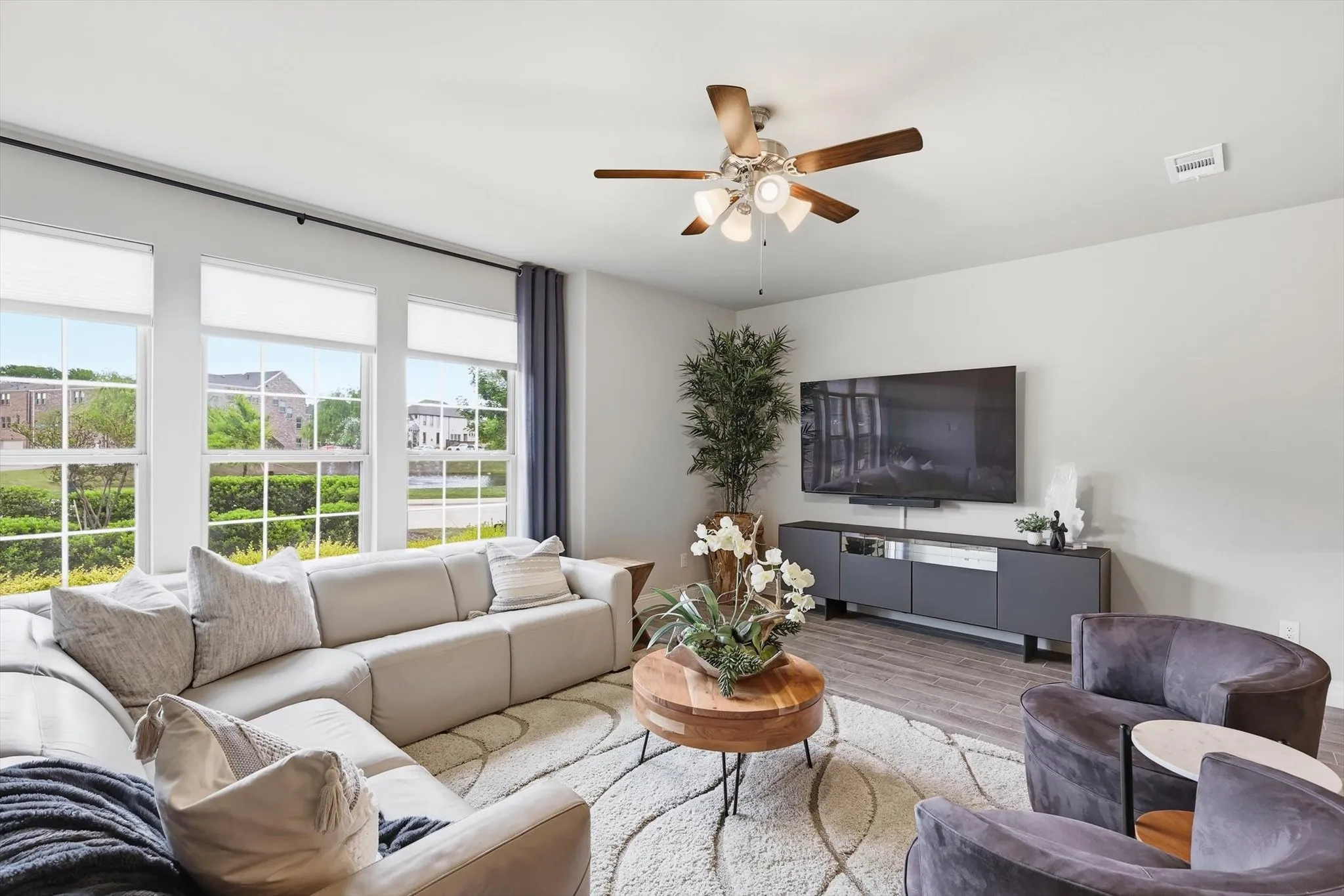 Living Room with a Spacious and Airy Layout, Generous Wall Width, and Large Rectangular Walls ideal for Mounted Installations or Decorative Treatments. A Centered Ceiling Fan, Large Windows, and Power Blinds provide Functional Airflow, Abundant Natural Light, and Privacy, creating a Modern Architectural Feel with High Ceilings, Open Floor Space, and a Neutral Color Palette that supports Flexible Layout and Contemporary Design Styling.