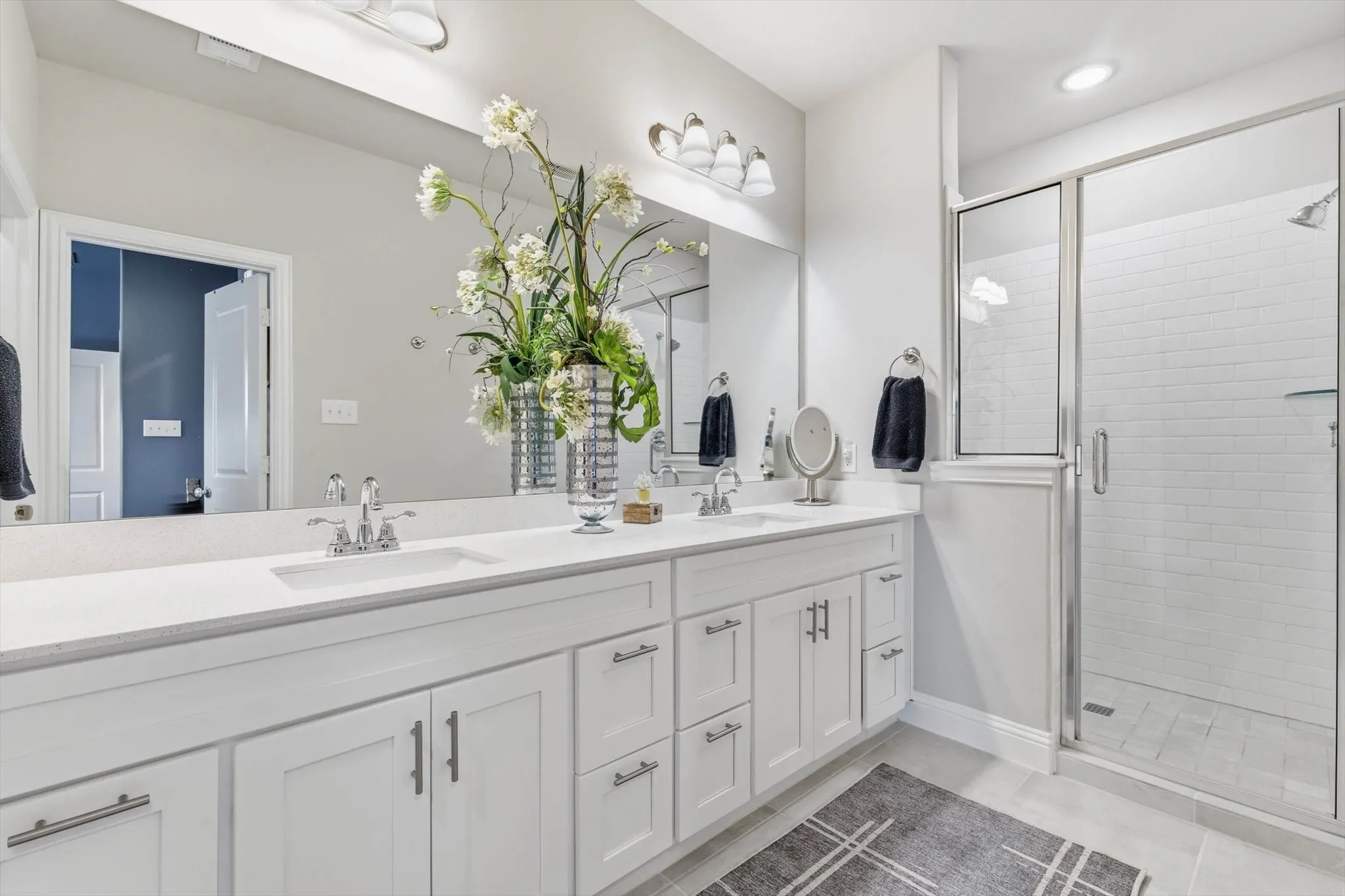 The Luxurious Primary Bathroom features a Raised Mirrored Vanity, Dual Sinks, Quartz Countertops, Designer Lighting, Upgraded Tile Flooring, and a Large Tile Shower.