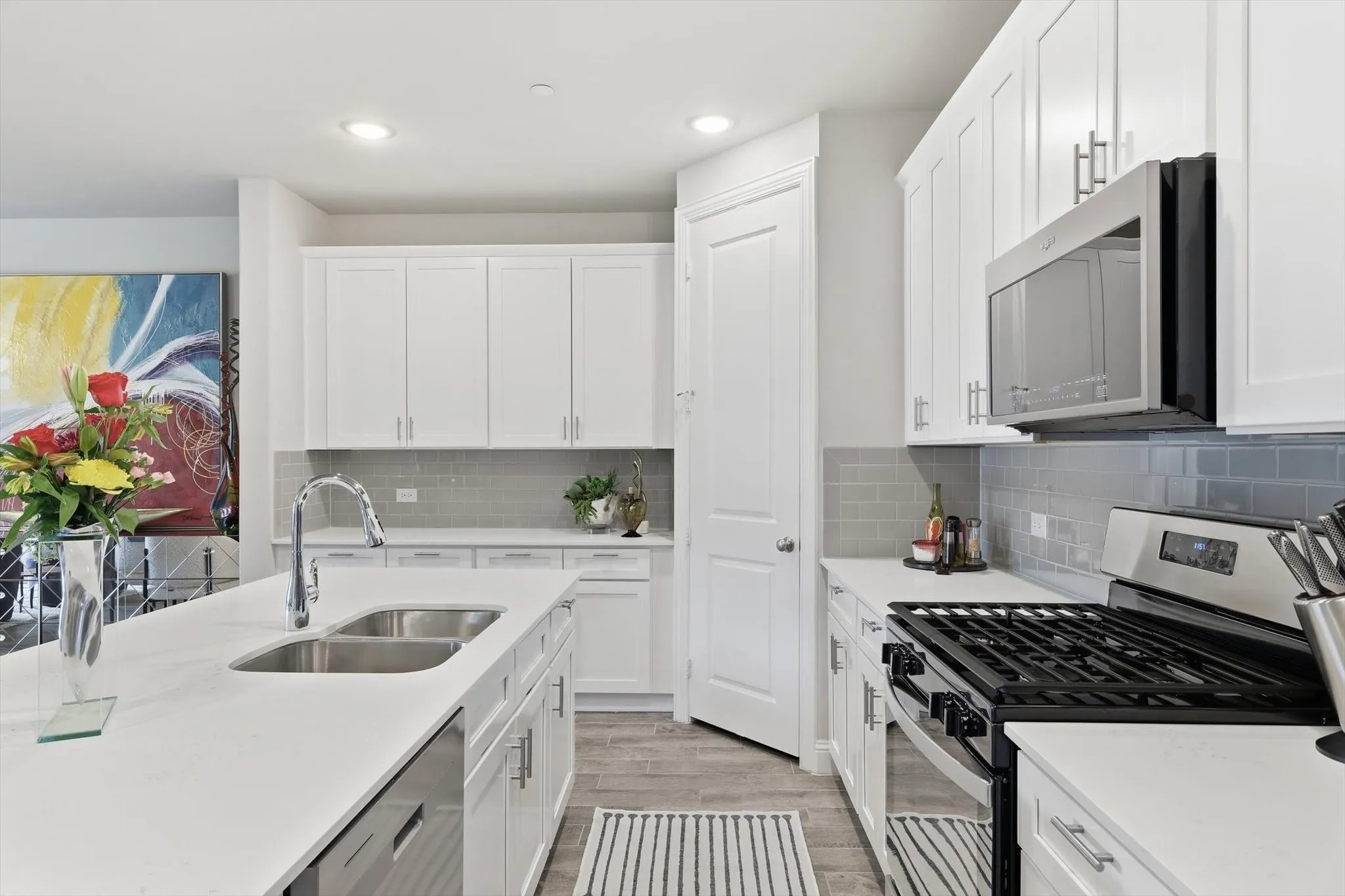. The Cook’s Kitchen showcases Modern White Shaker-Style Cabinetry, Light-Toned Quartz Countertops, a Spacious Center Island with Breakfast Bar, Soft Gray Subway Tile Backsplash, Recessed Lighting, and Upgraded Wood-Look Tile Flooring for Durability and Warmth. A Full-Height Pantry and Multiple Work Zones enhance Functionality and Flow, seamlessly connecting the Living and Dining Areas for Effortless Entertaining