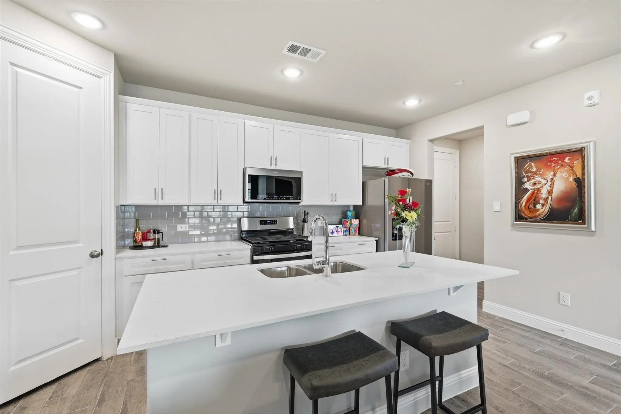 . The Cook’s Kitchen showcases Modern White Shaker-Style Cabinetry, Light-Toned Quartz Countertops, a Spacious Center Island with Breakfast Bar, Soft Gray Subway Tile Backsplash, Recessed Lighting, and Upgraded Wood-Look Tile Flooring for Durability and Warmth. A Full-Height Pantry and Multiple Work Zones enhance Functionality and Flow, seamlessly connecting the Living and Dining Areas for Effortless Entertaining