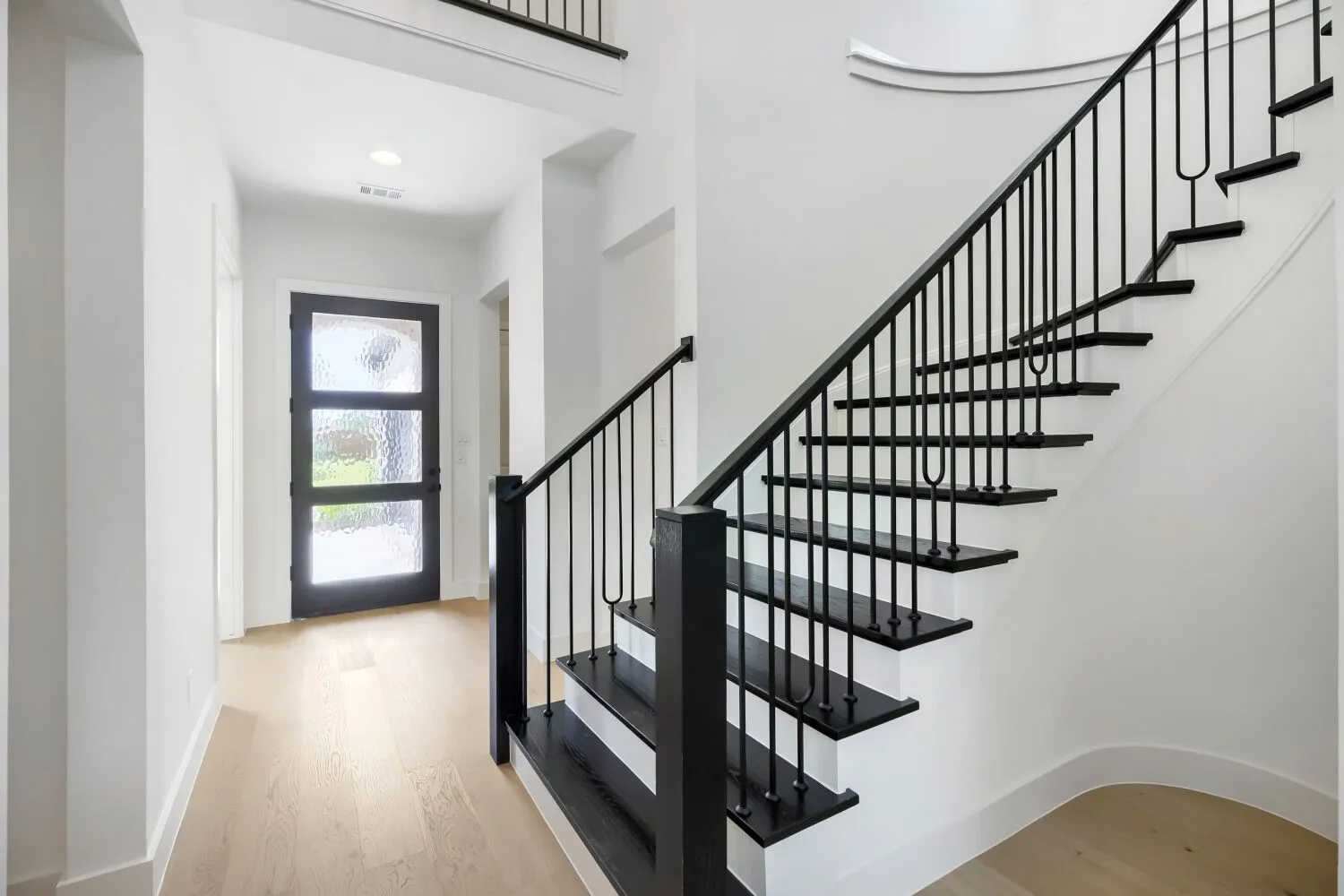 Entryway featuring light wood-finish flooring, a dark wood-finish door with frosted glass panels, and a staircase with dark wood-finish treads and black metal balusters
