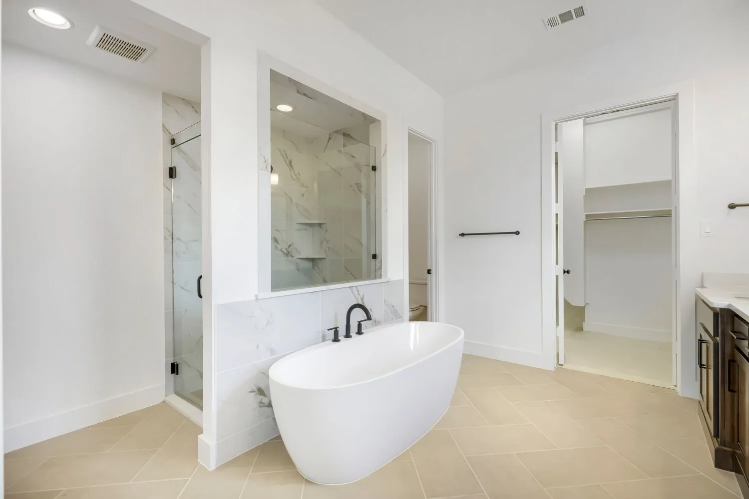 Freestanding soaking tub with matte black fixtures, glass-enclosed shower with marble-look tile, herringbone-patterned floor tiles, recessed lighting, and a dark wood vanity with a light countertop