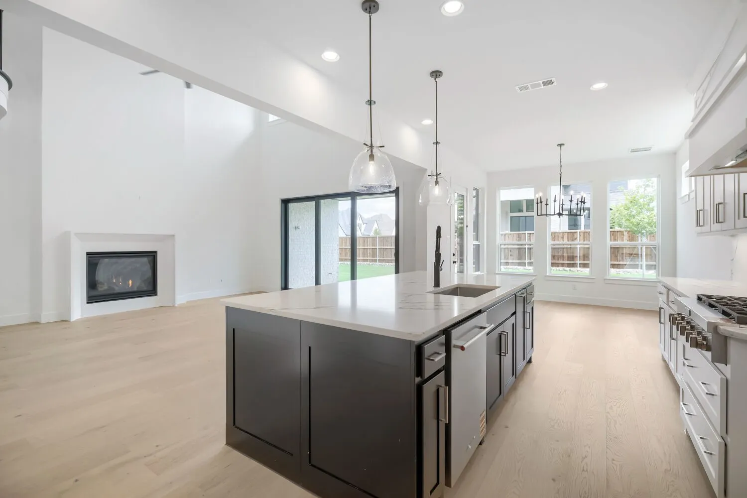 Spacious open-concept kitchen and living area featuring high ceilings, light wood-finish flooring, and a contemporary fireplace