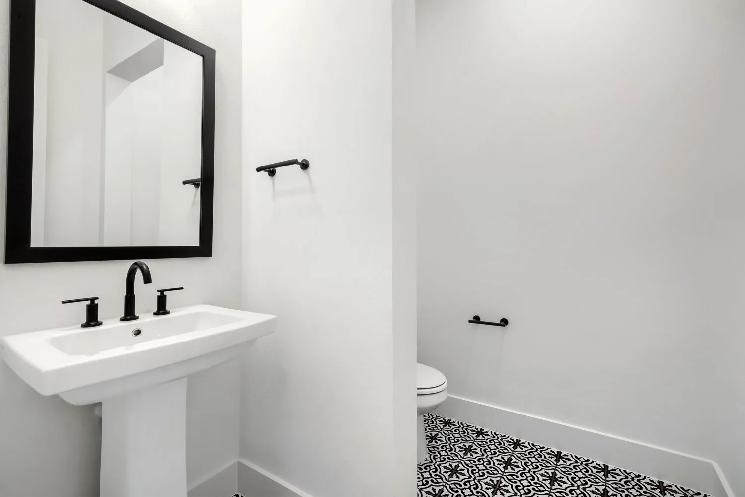 Pedestal sink featuring a matte black faucet and coordinating framed mirror
