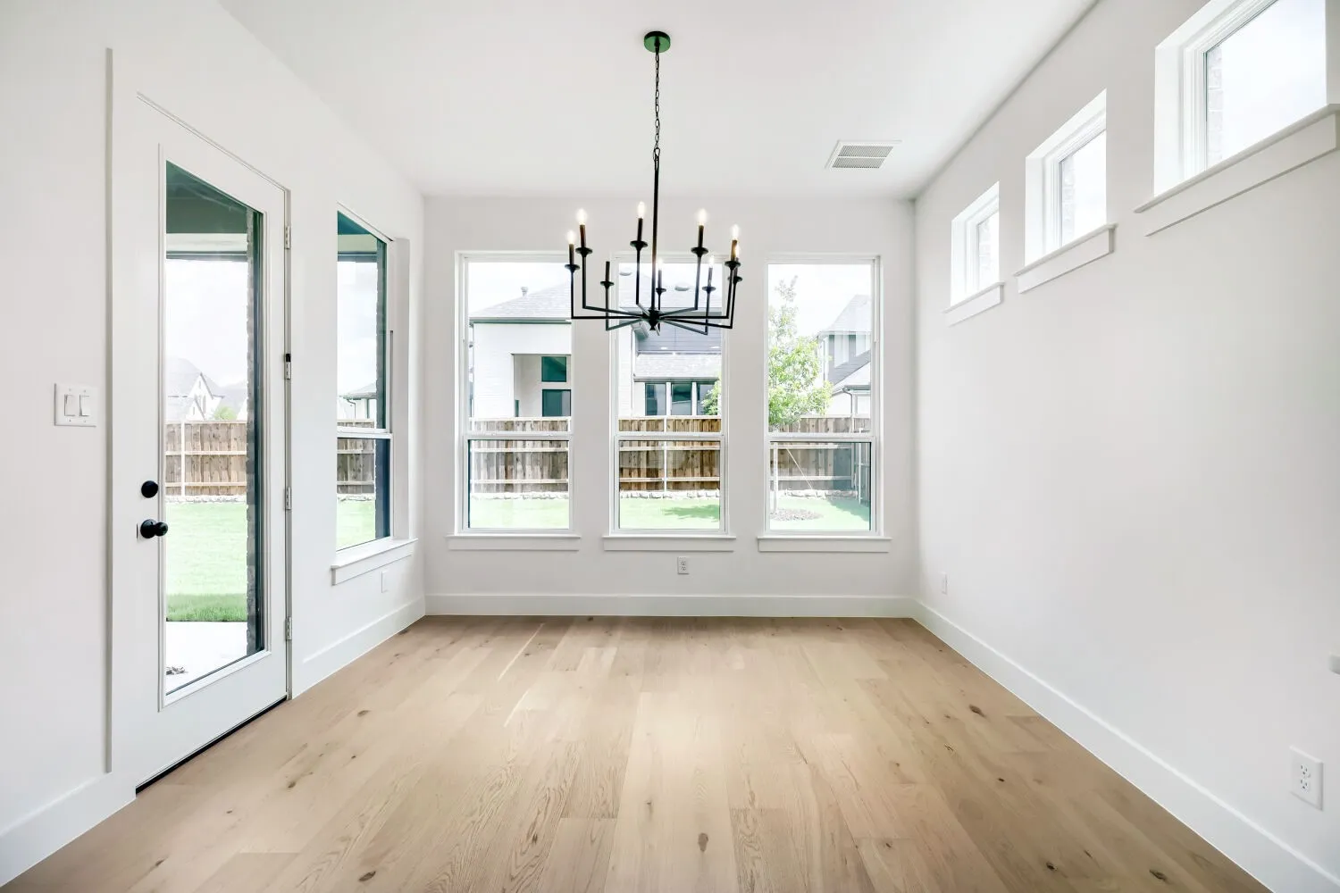 Room featuring wood-finish flooring, a contemporary black chandelier, and multiple windows