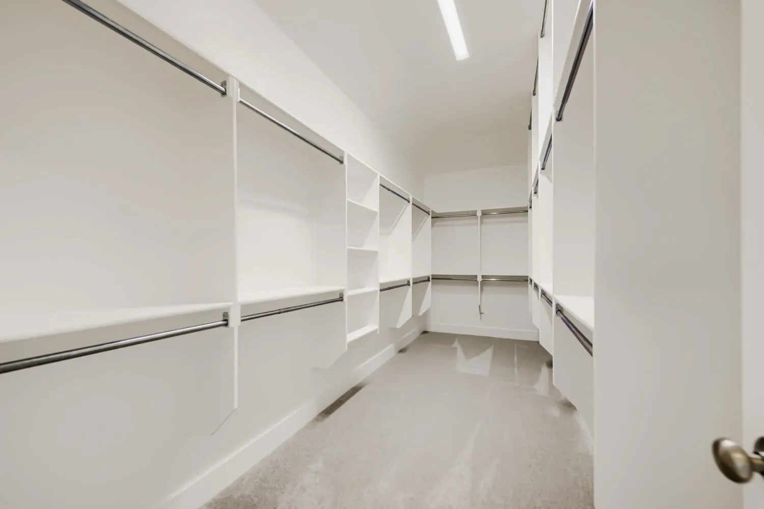 Spacious walk-in closet featuring extensive built-in shelving, multiple hanging rods, and light-colored flooring