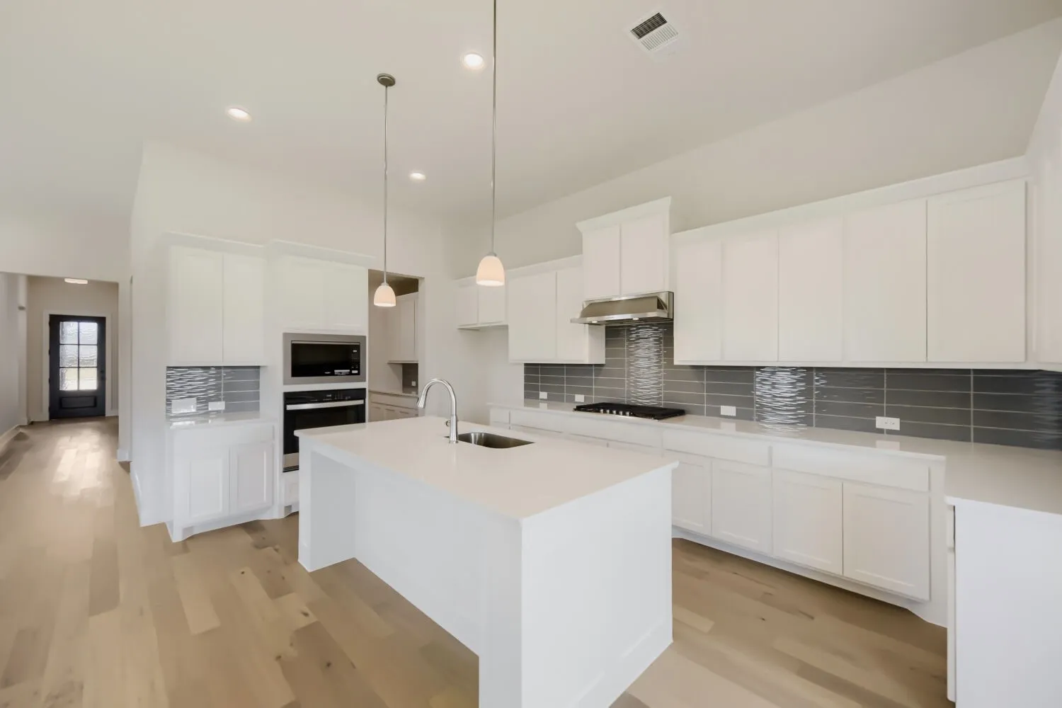 Kitchen featuring white shaker cabinetry, an expansive island with an undermount sink, integrated stainless steel appliances, a tile backsplash, and wood-finish flooring