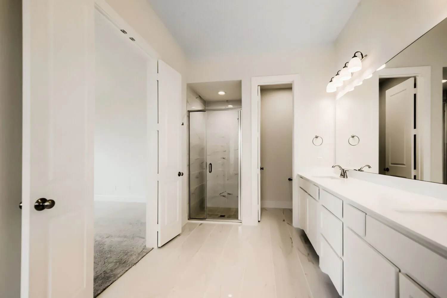 Spacious bathroom featuring a double vanity with ample storage, a large wall-mounted mirror, and a walk-in shower with clear glass enclosure