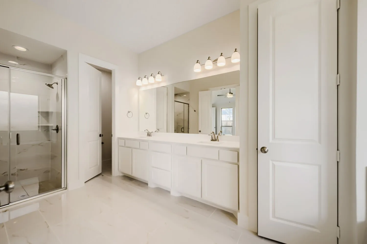 Spacious bathroom featuring a double vanity with white cabinetry, a large mirror, and a glass-enclosed shower with tiled walls and a built-in shelf