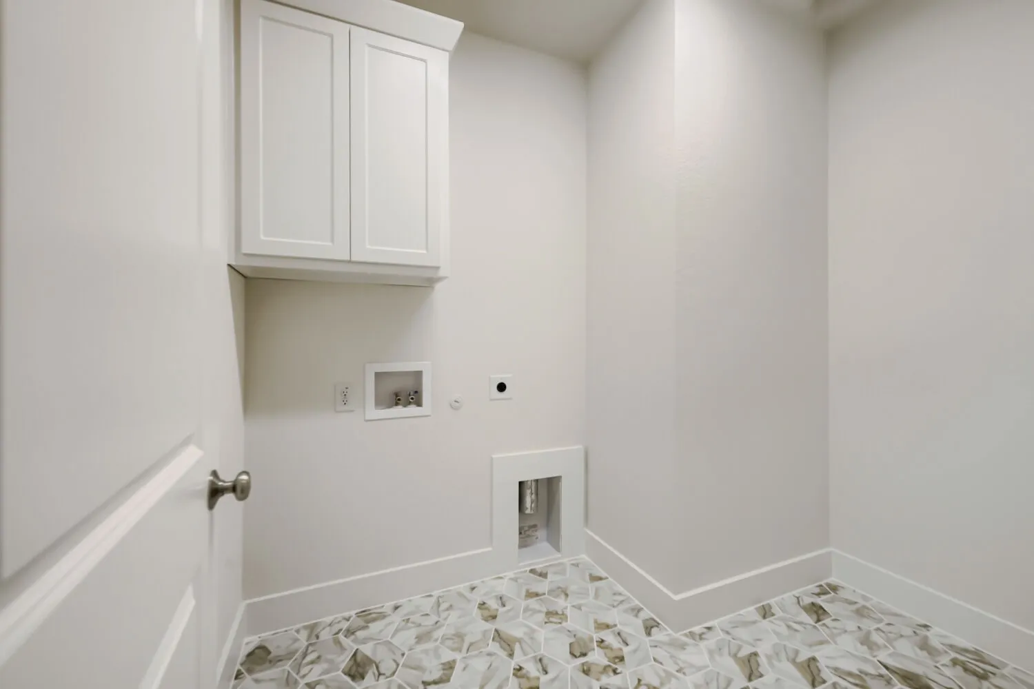 Laundry room featuring white shaker-style cabinetry, patterned floor tiling, and a neutral wall palette