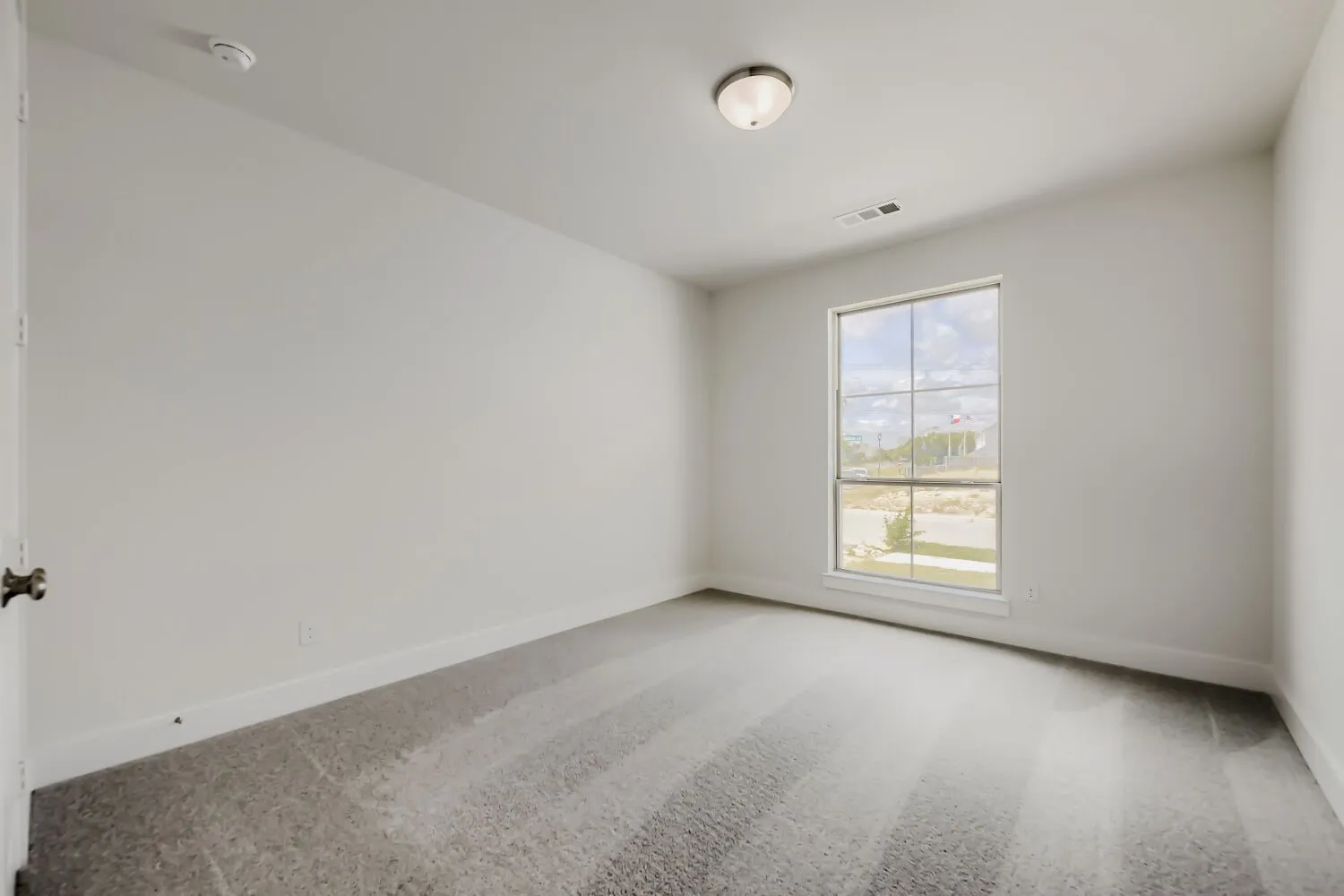 Bright room with a large window, neutral gray carpet, white baseboards, and a flush-mount ceiling light fixture