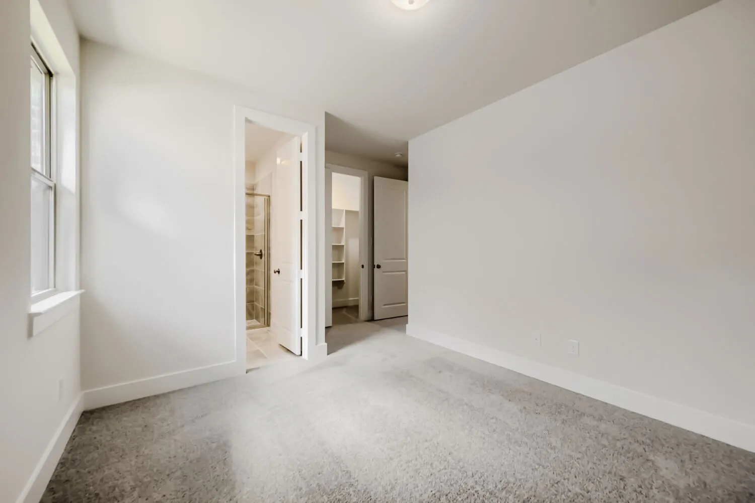 Carpeted room with a double-hung window and a doorway leading to a tiled bathroom with a glass-enclosed shower