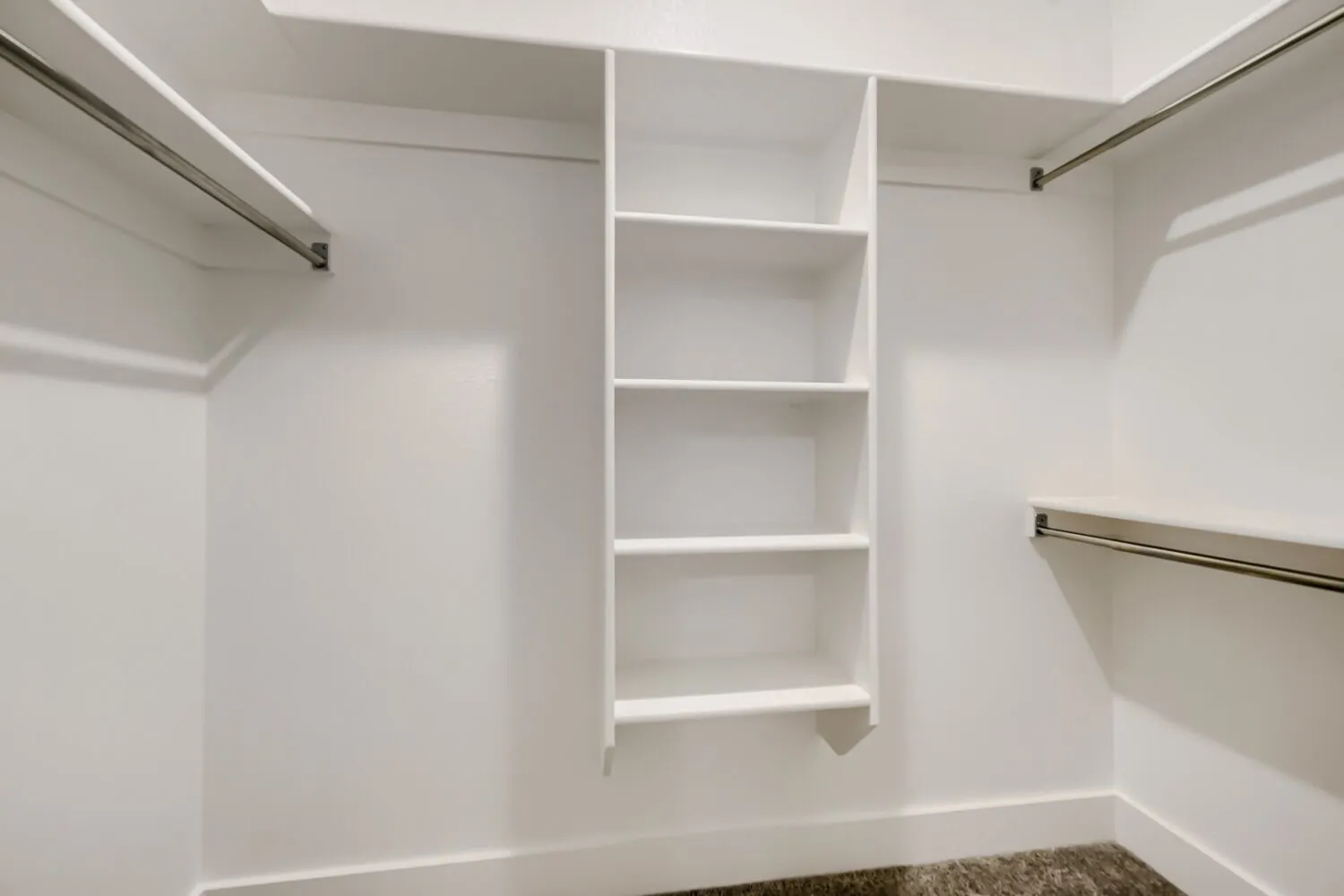 Walk-in closet featuring white built-in shelving, multiple hanging rods, and perimeter baseboards