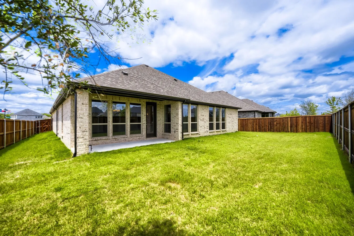 Expansive backyard featuring a lush lawn, privacy fencing, and a covered patio