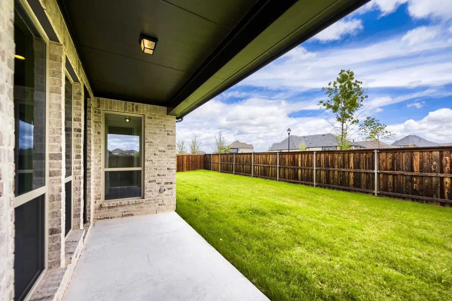 Covered concrete patio overlooking a fenced backyard with a manicured lawn