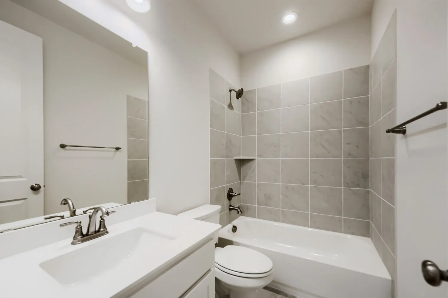 Bathroom featuring a white vanity with an integrated sink, a large wall-mounted mirror, a toilet, and a shower-tub combination with light grey tile surround