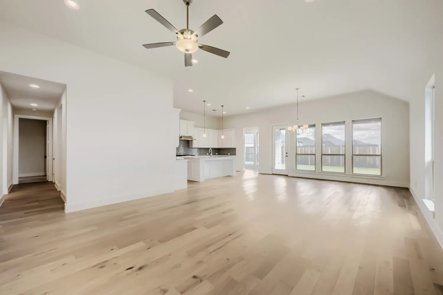Spacious open-concept interior featuring light wood-finish flooring, recessed lighting, and a contemporary ceiling fan
