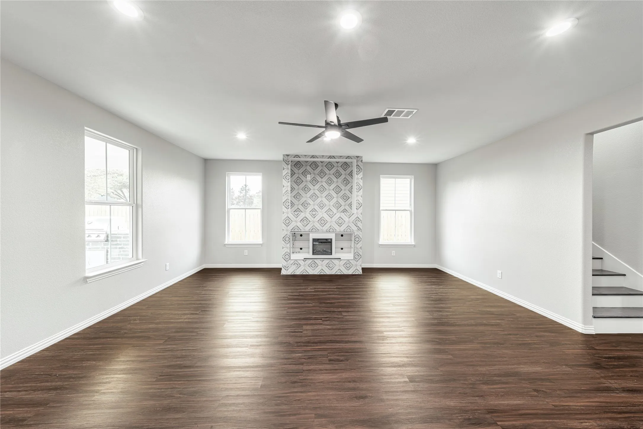 Unfurnished living room with dark wood-type flooring, ceiling fan, recessed lighting, healthy amount of natural light, and a tiled fireplace