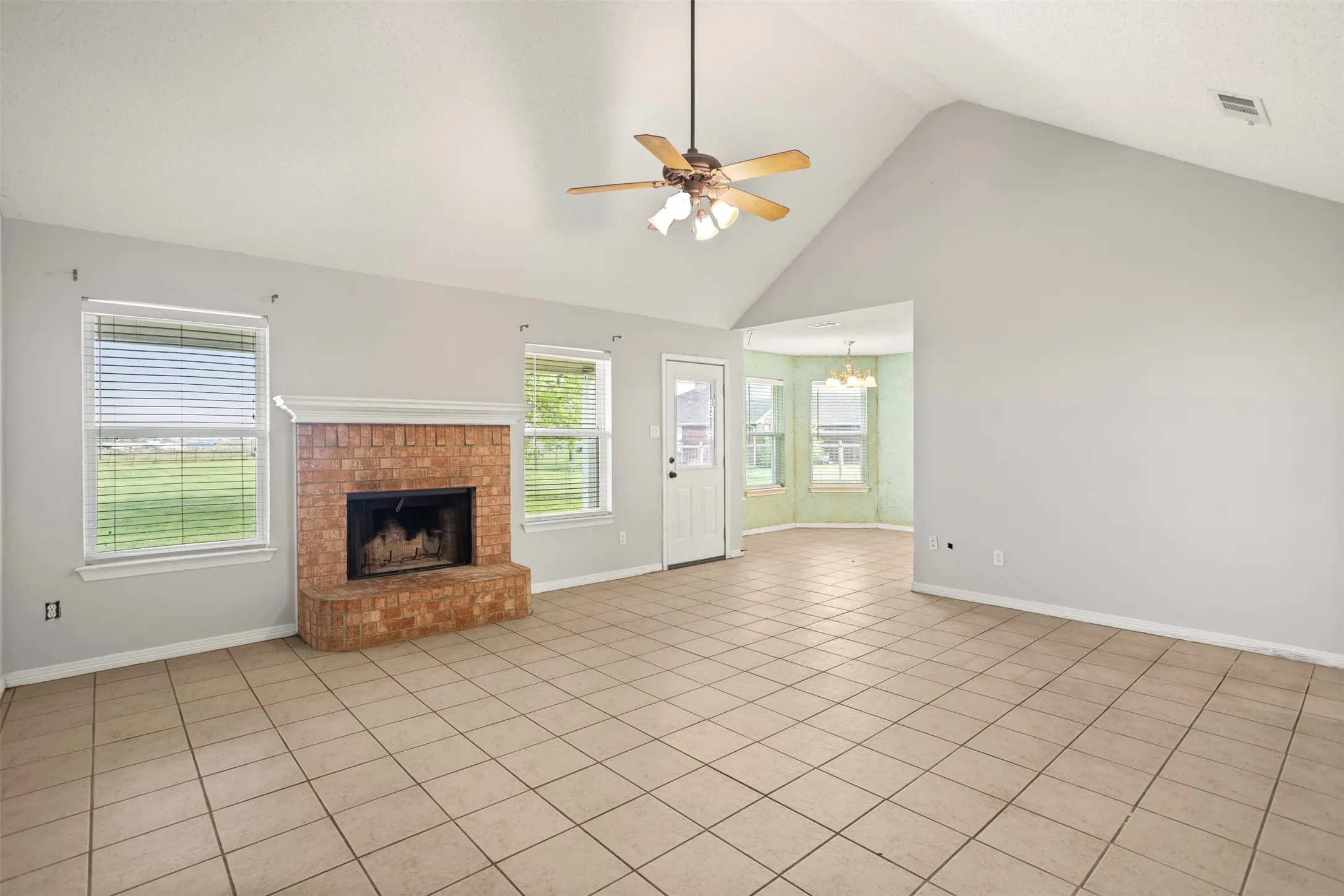 Unfurnished living room with a ceiling fan, light tile patterned flooring, a high ceiling, a fireplace, and a chandelier