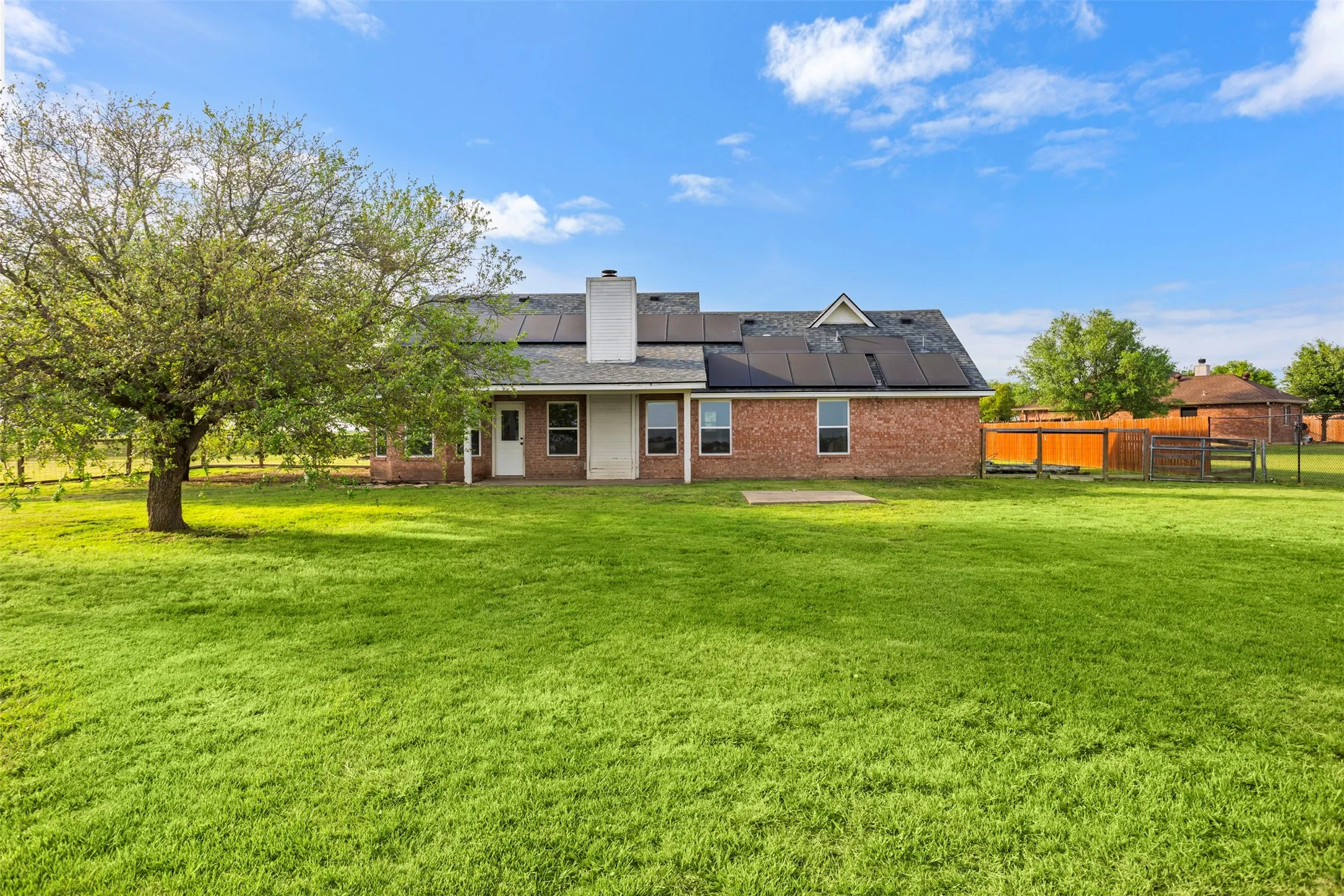 Rear view of property with roof mounted solar panels, a patio area, a chimney, brick siding, and a fenced backyard