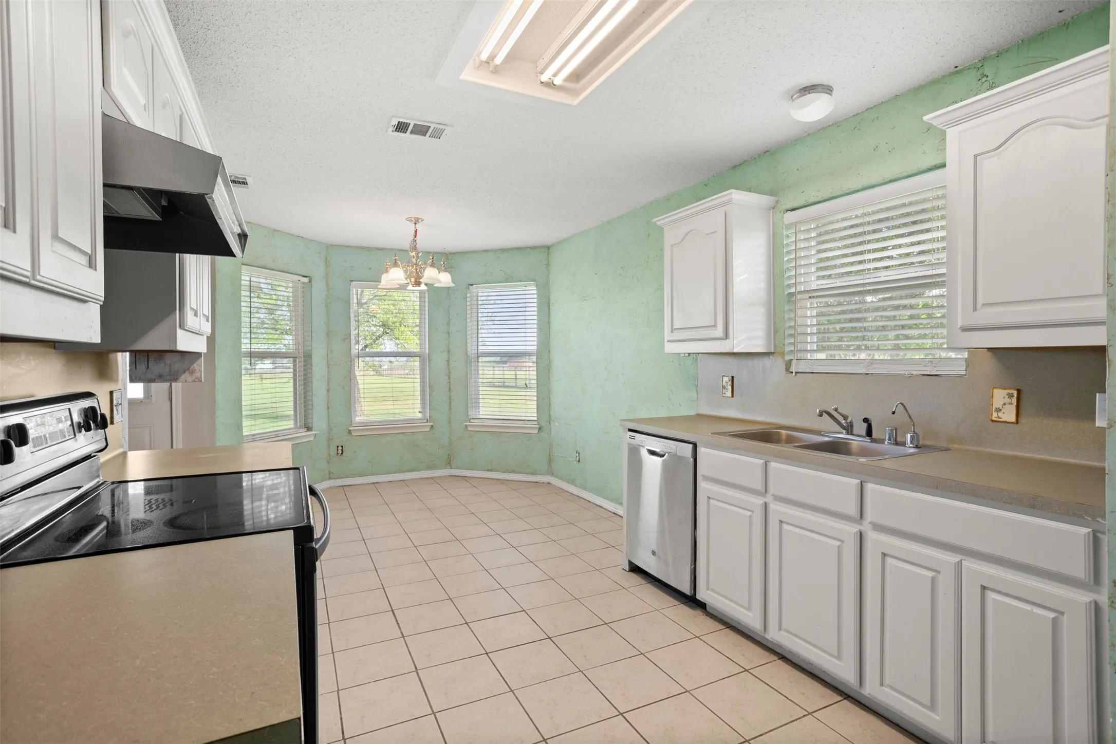 Kitchen with stainless steel appliances, a chandelier, white cabinetry, a textured ceiling, and light countertops