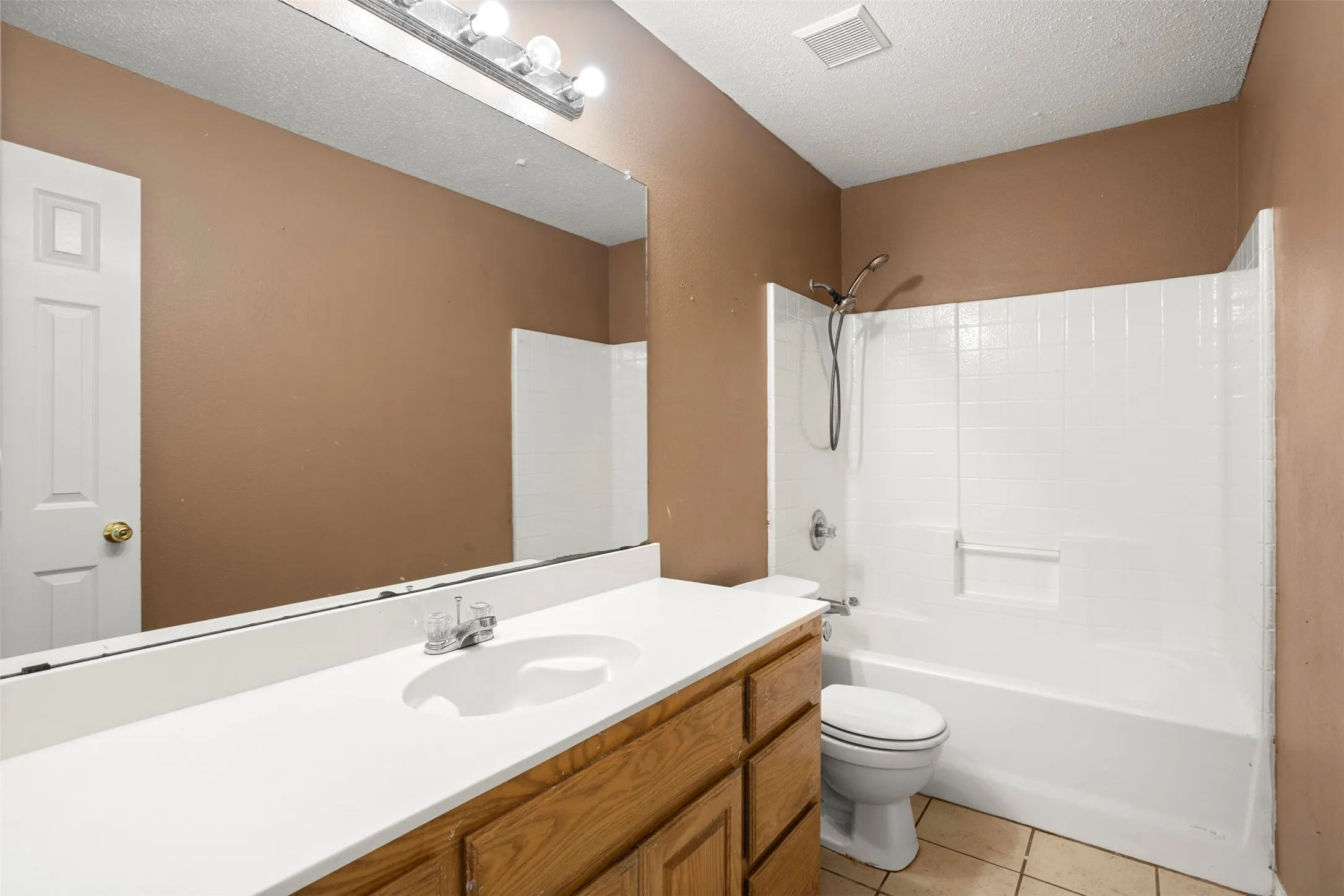 Bathroom featuring vanity, light tile patterned floors, bathtub / shower combination, and a textured ceiling