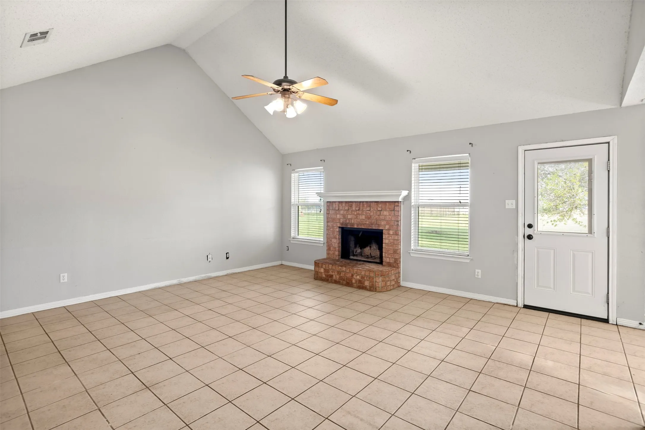 Unfurnished living room featuring a high ceiling, a fireplace, a ceiling fan, and light tile patterned floors
