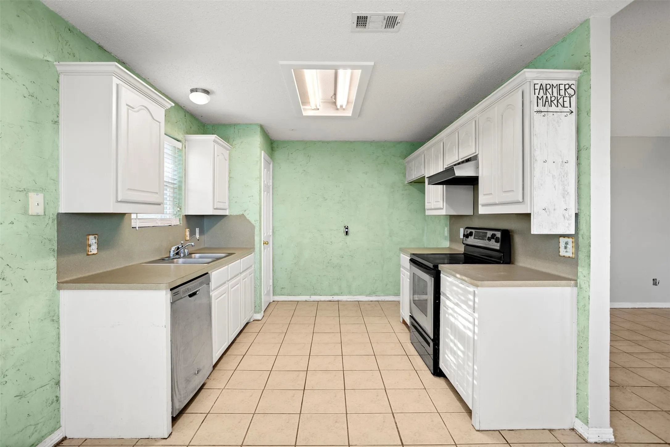 Kitchen with stainless steel appliances, light countertops, white cabinets, and light tile patterned floors