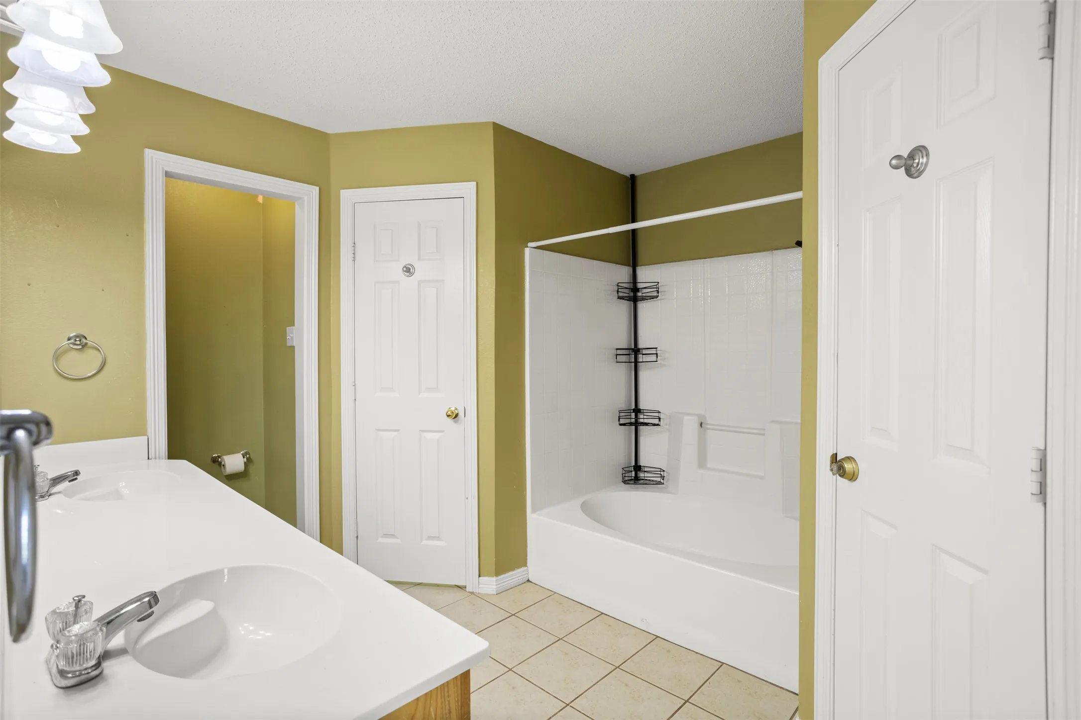 Full bath with double vanity, light tile patterned floors, shower / bathtub combination, and a textured ceiling